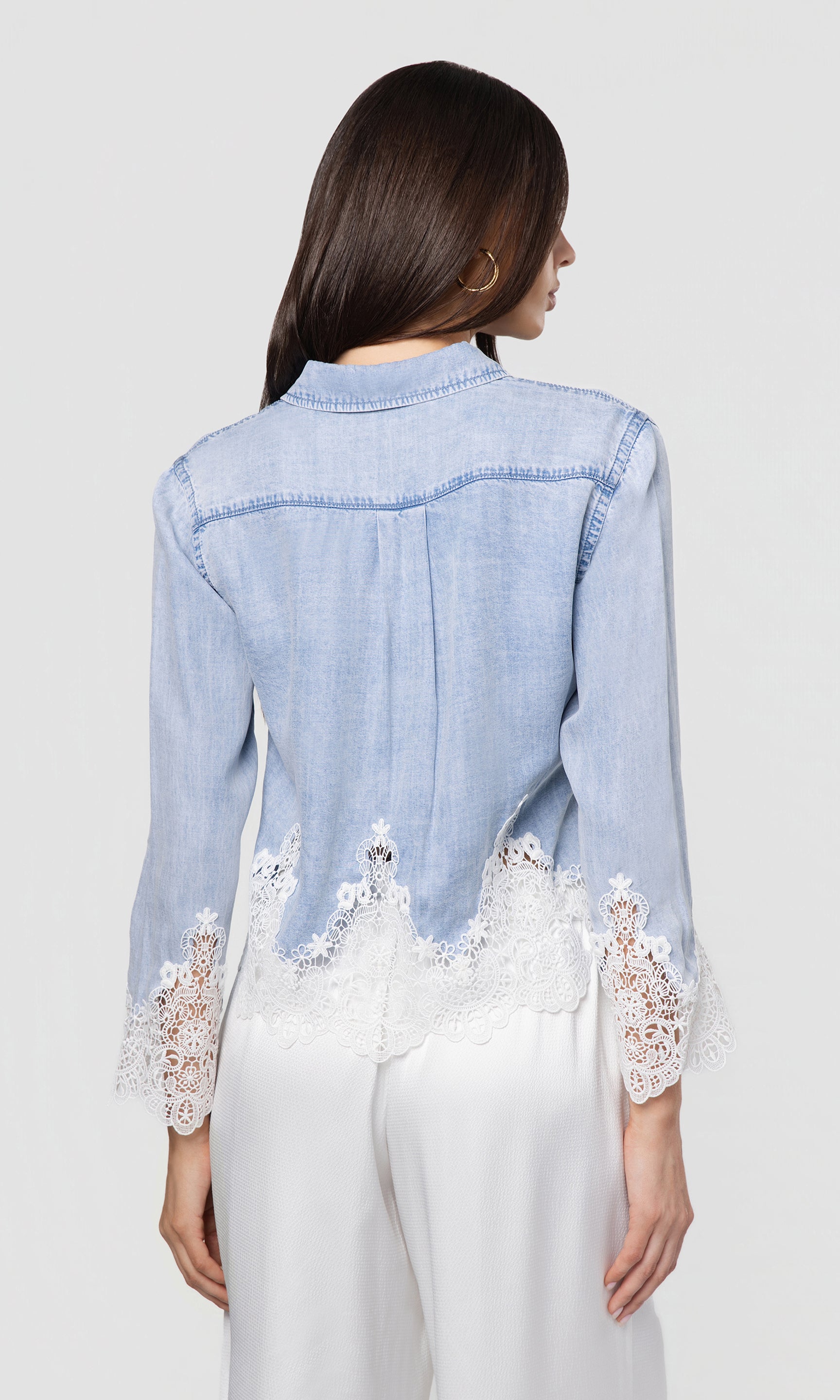 Back view of light blue denim shirt with lace details worn by a person on a white background