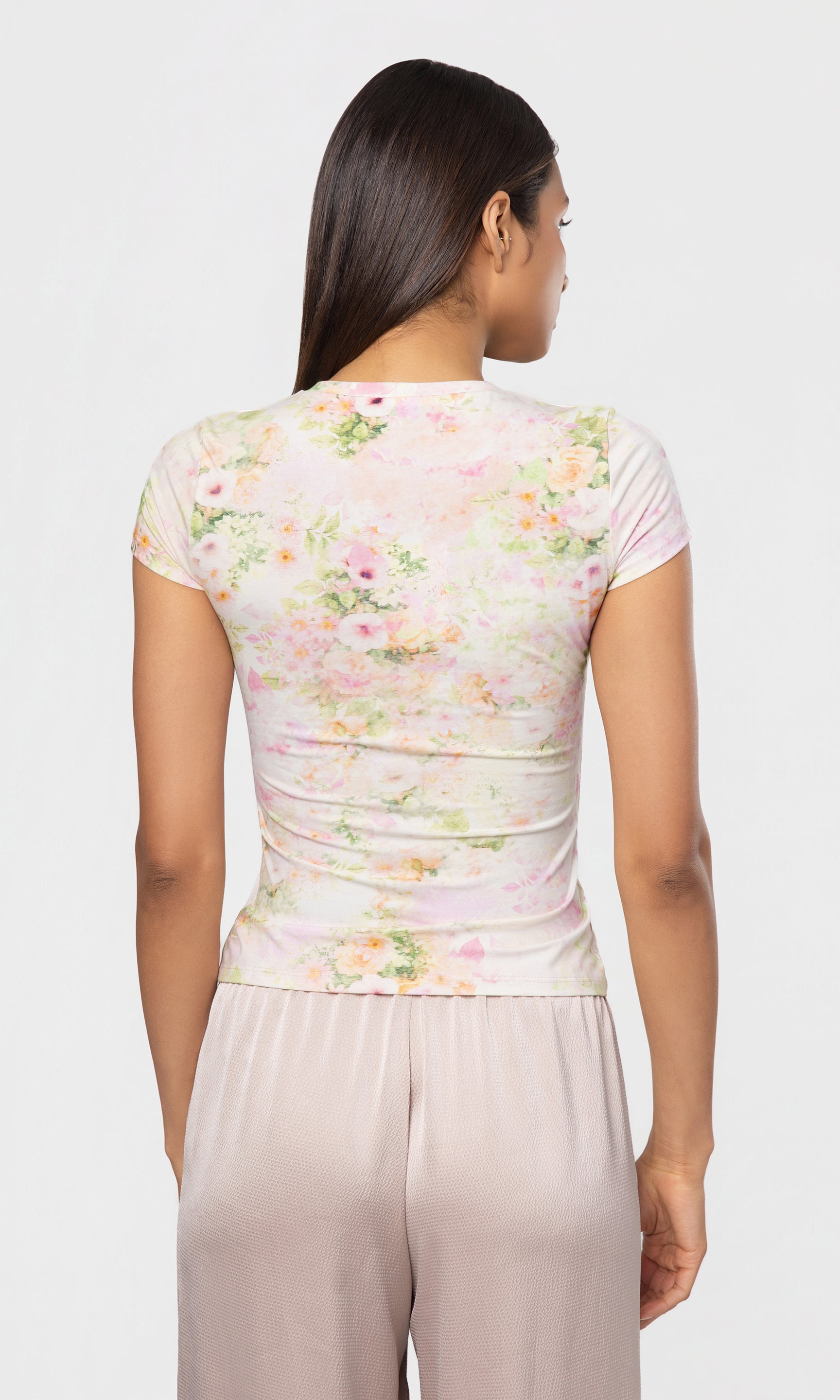 Back view of woman wearing a floral top and beige pants on a white background