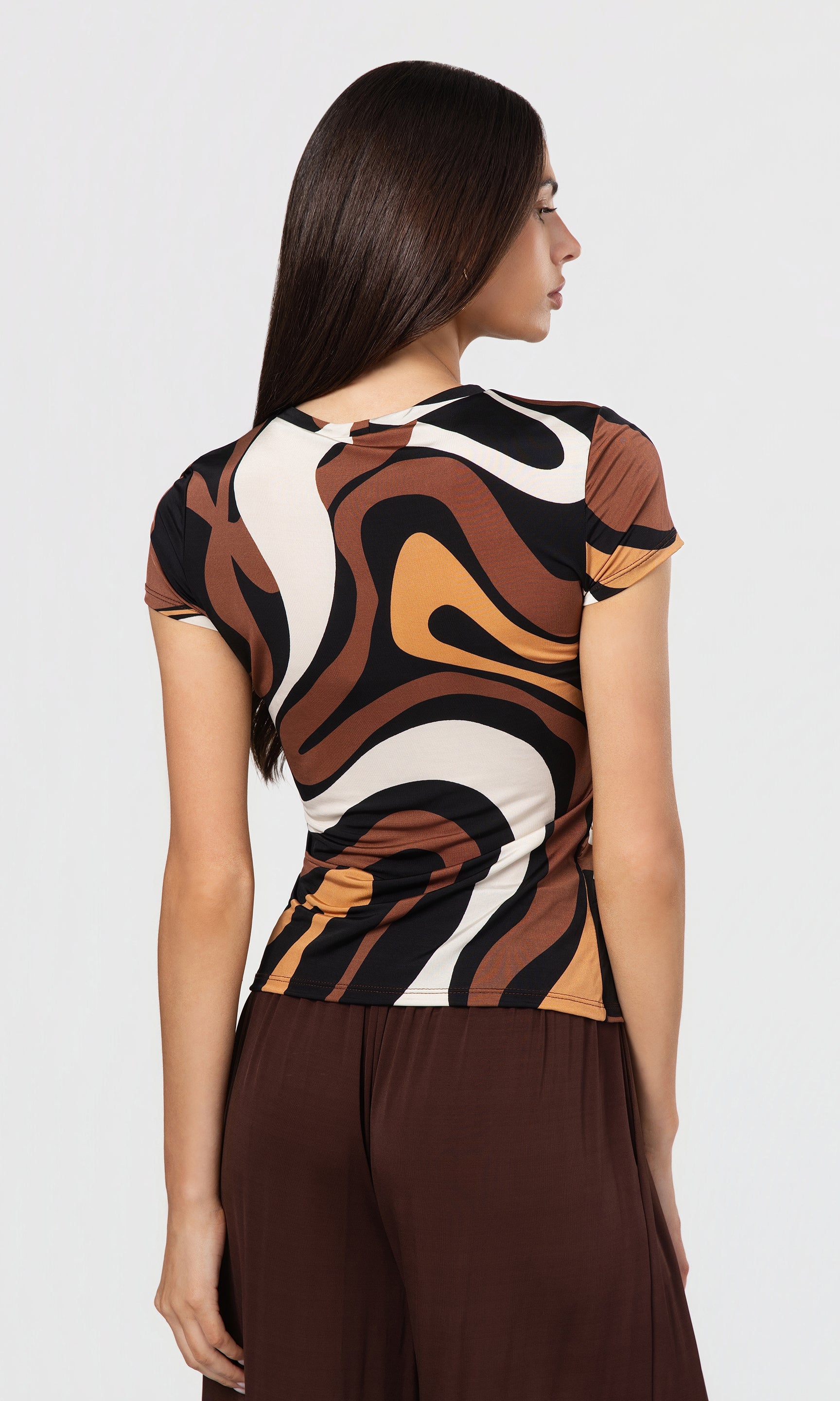 Back view of woman wearing a patterned top and brown pants on a white background