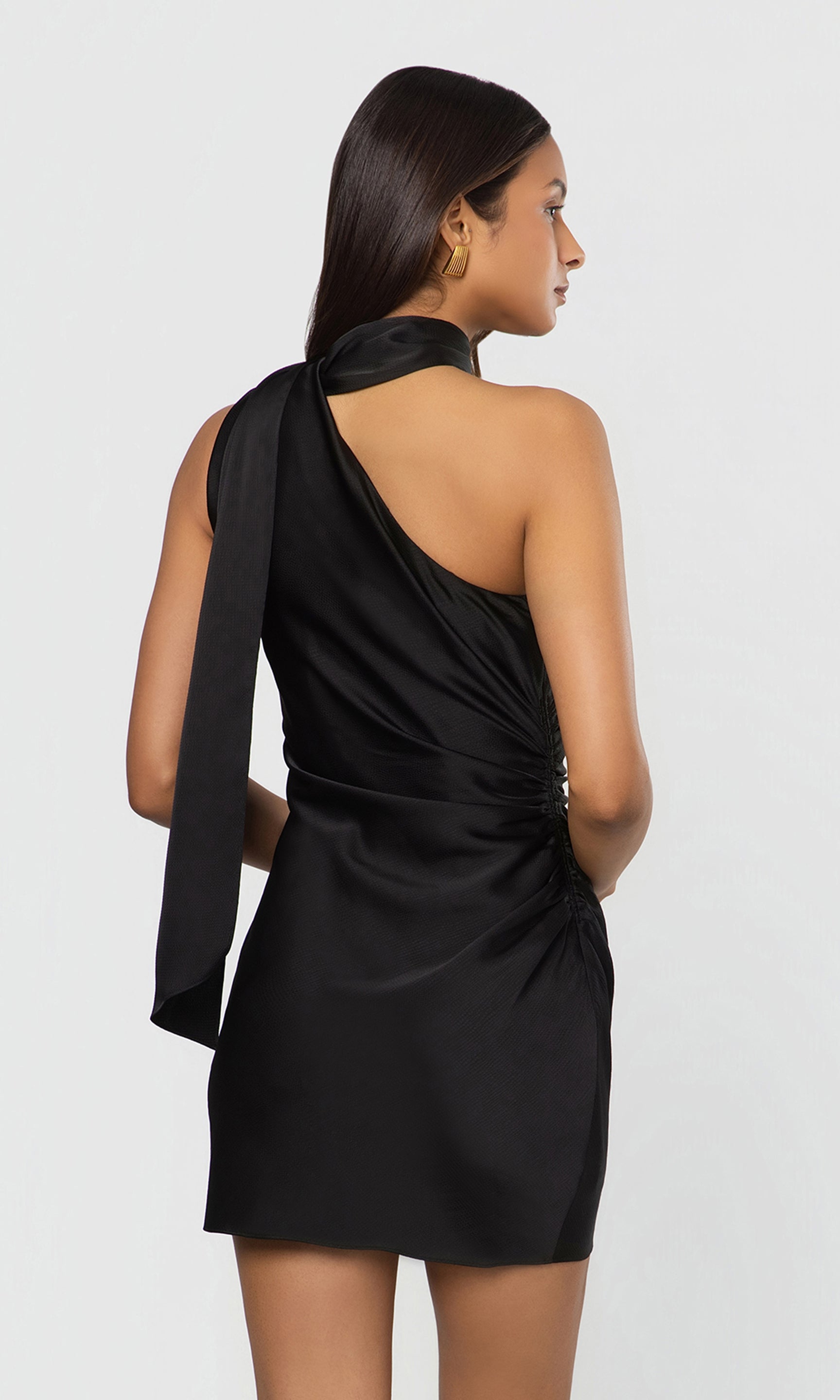 Back view of woman wearing a black one-shoulder dress against a white background