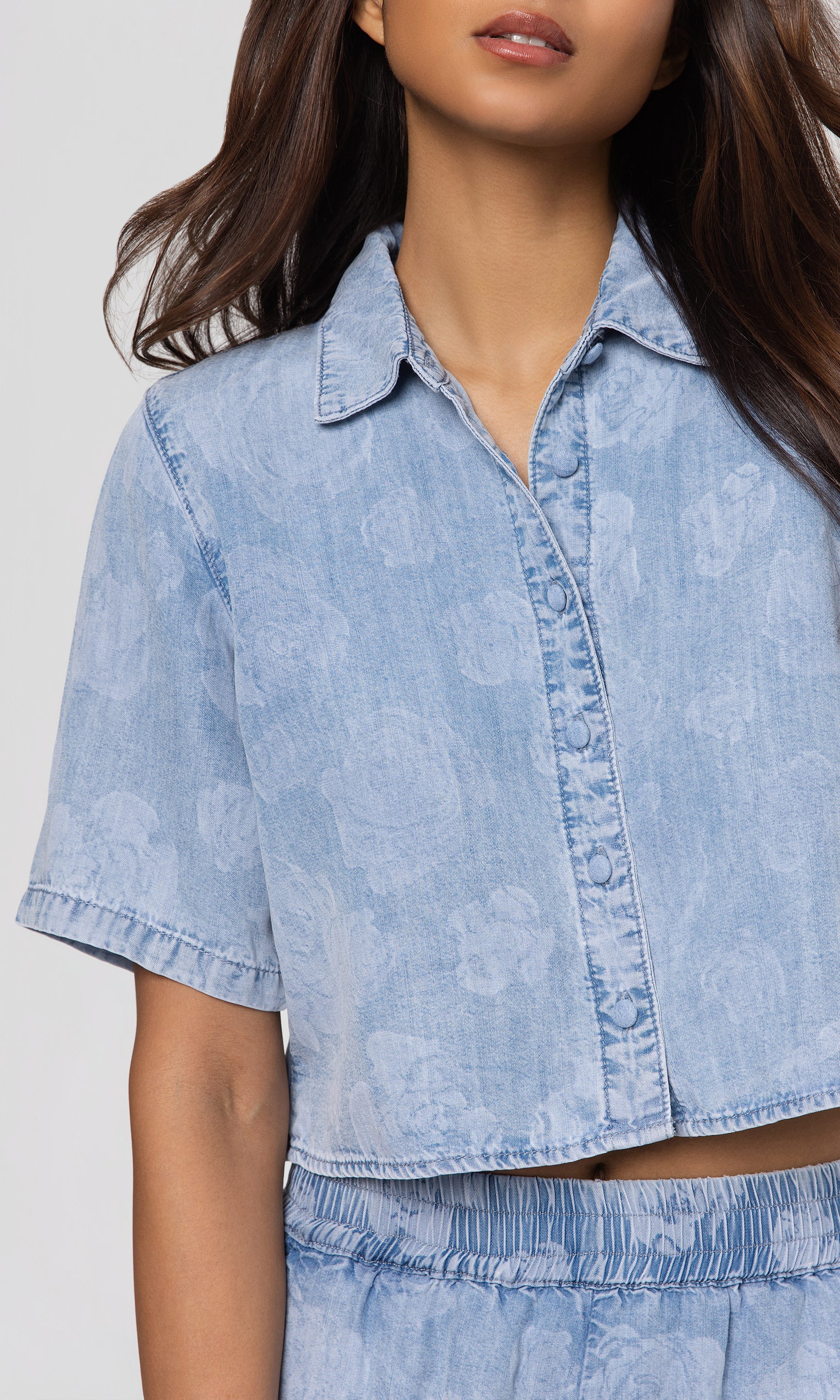 Close-up of light blue denim shirt worn by a person on a white background