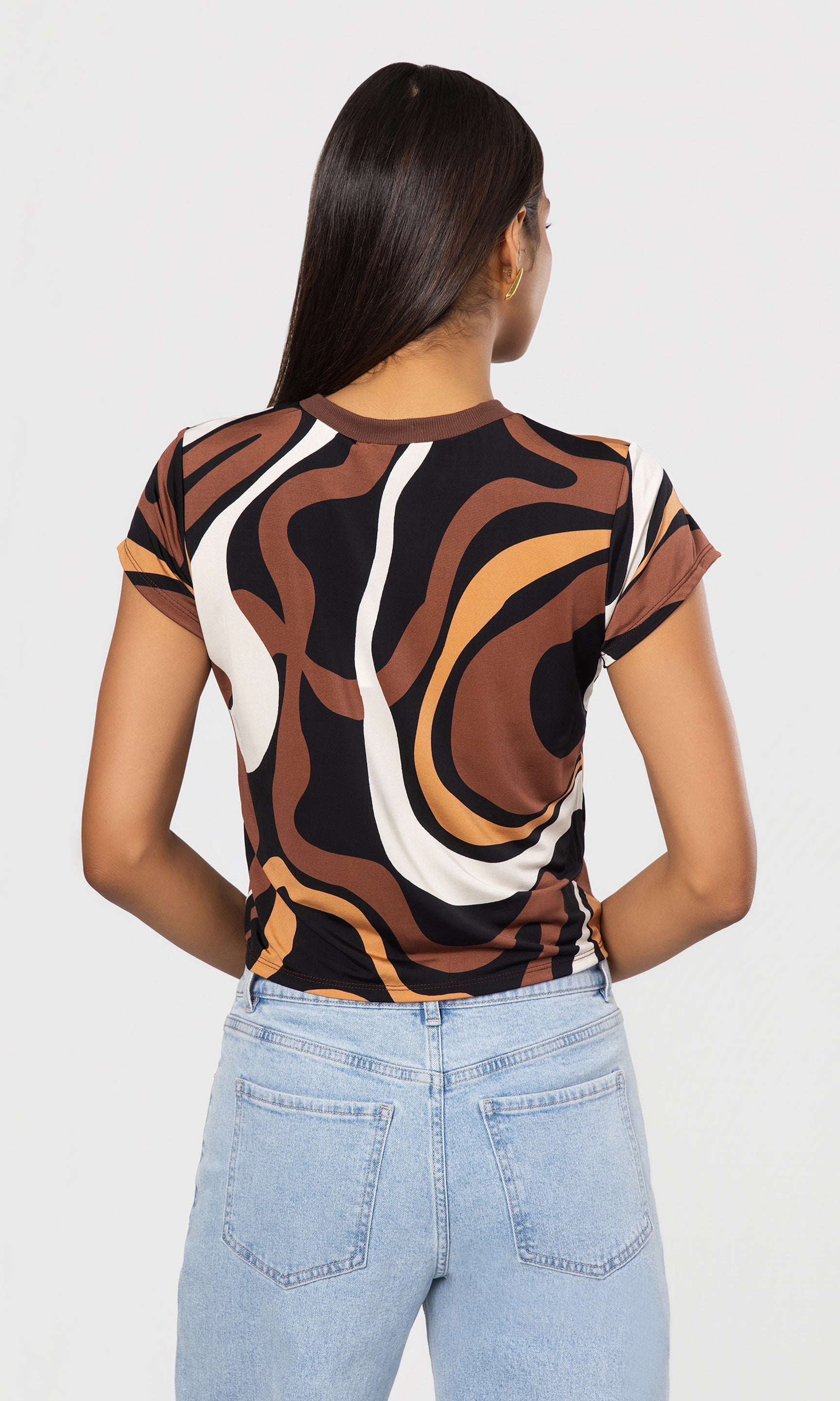 back view of person wearing a patterned top and light blue jeans on a white background