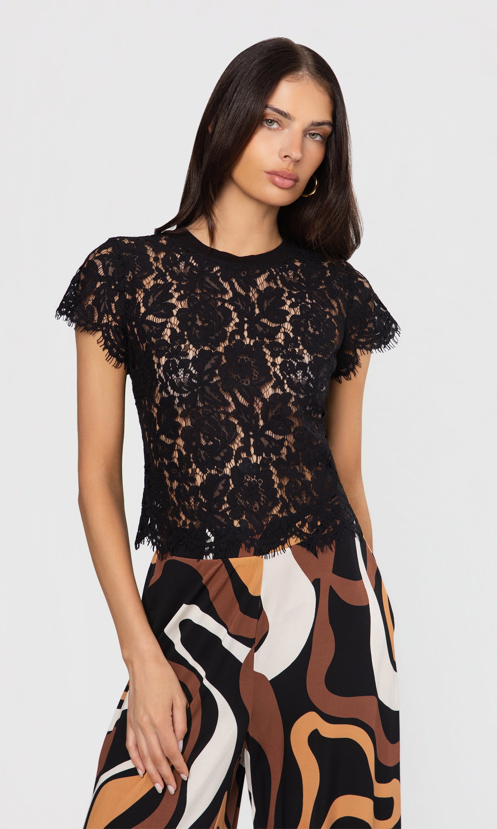 Woman wearing a black lace top and patterned pant on a white background
