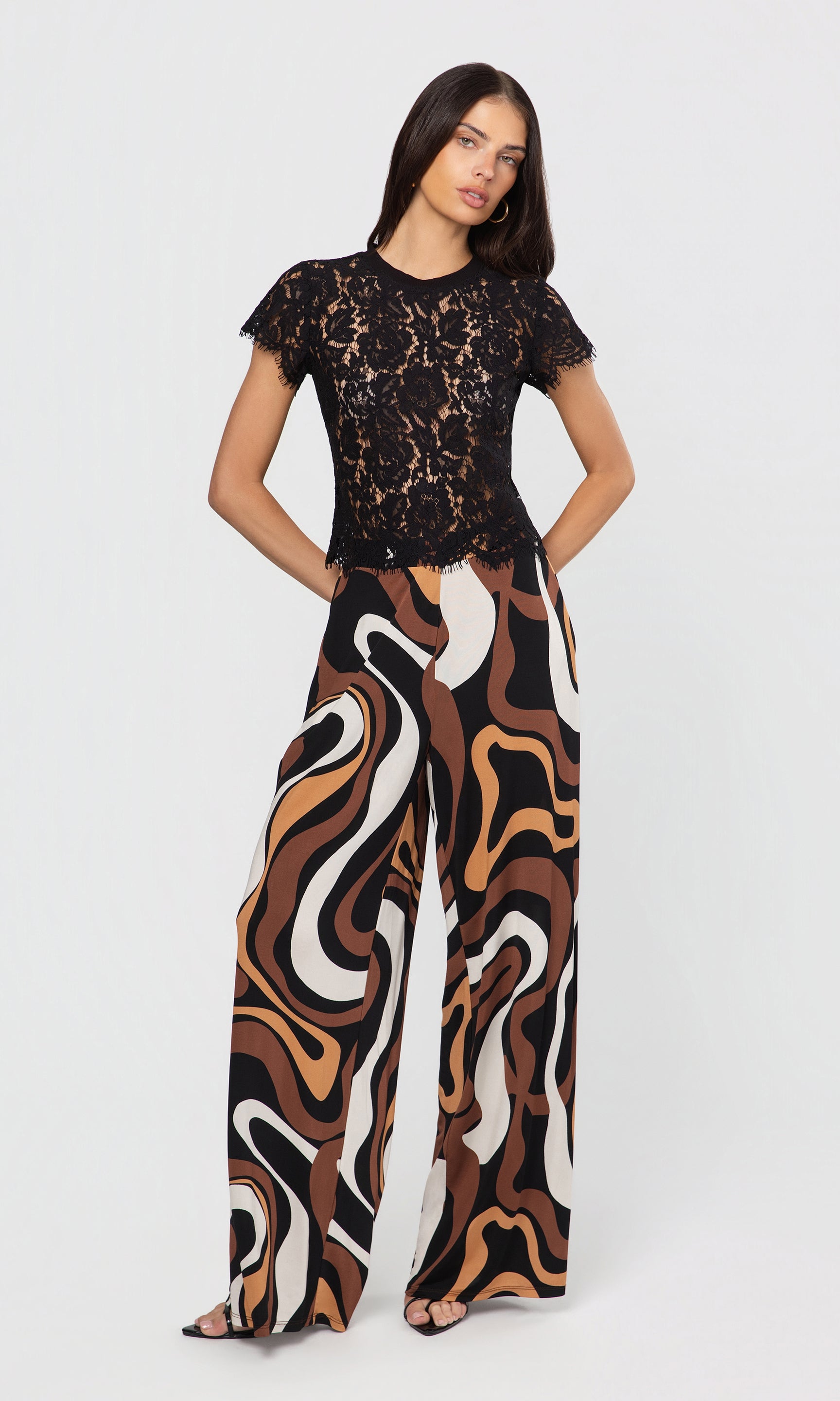 Woman wearing a black lace top and patterned pants on a white background