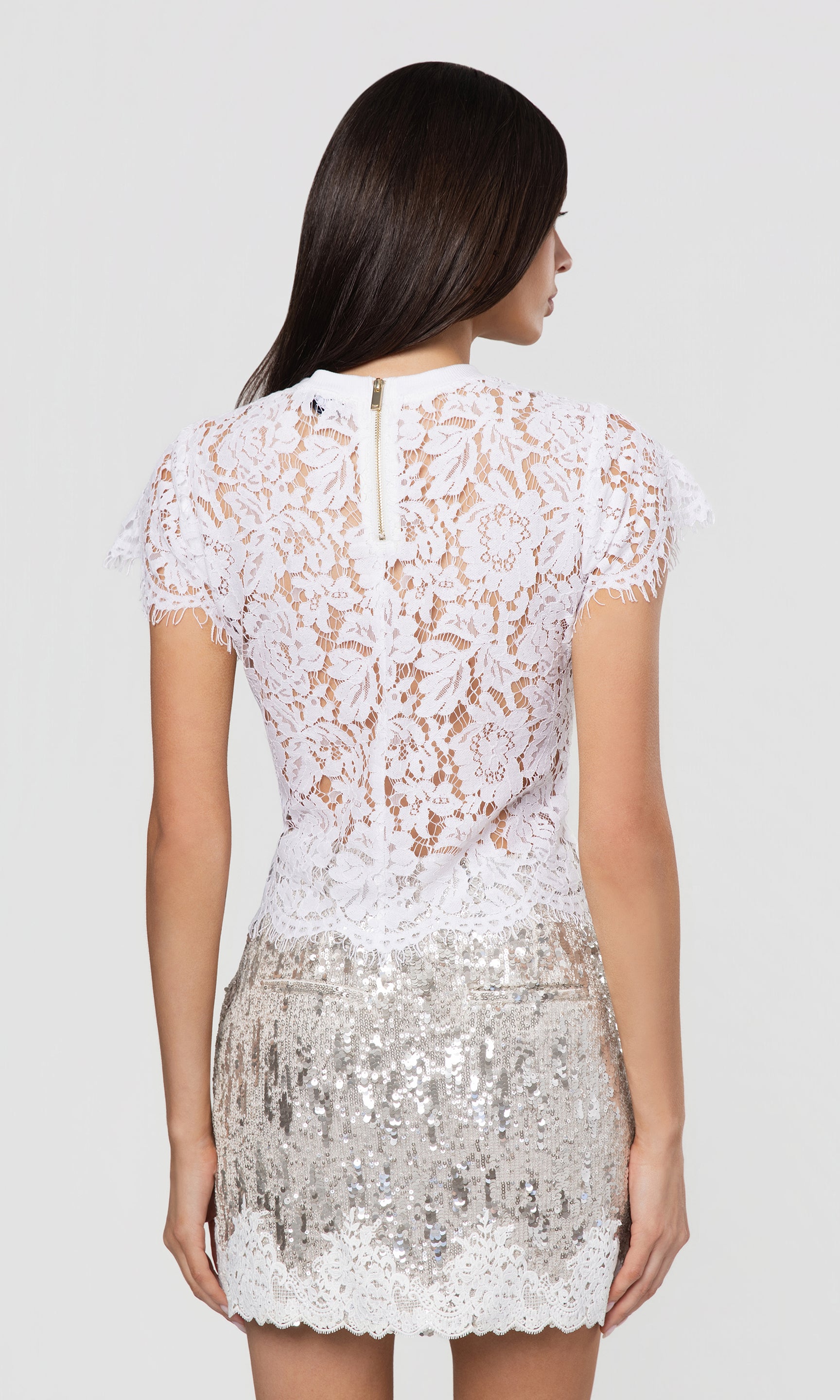 Back view of white lace top with silver sequin skirt on a white background