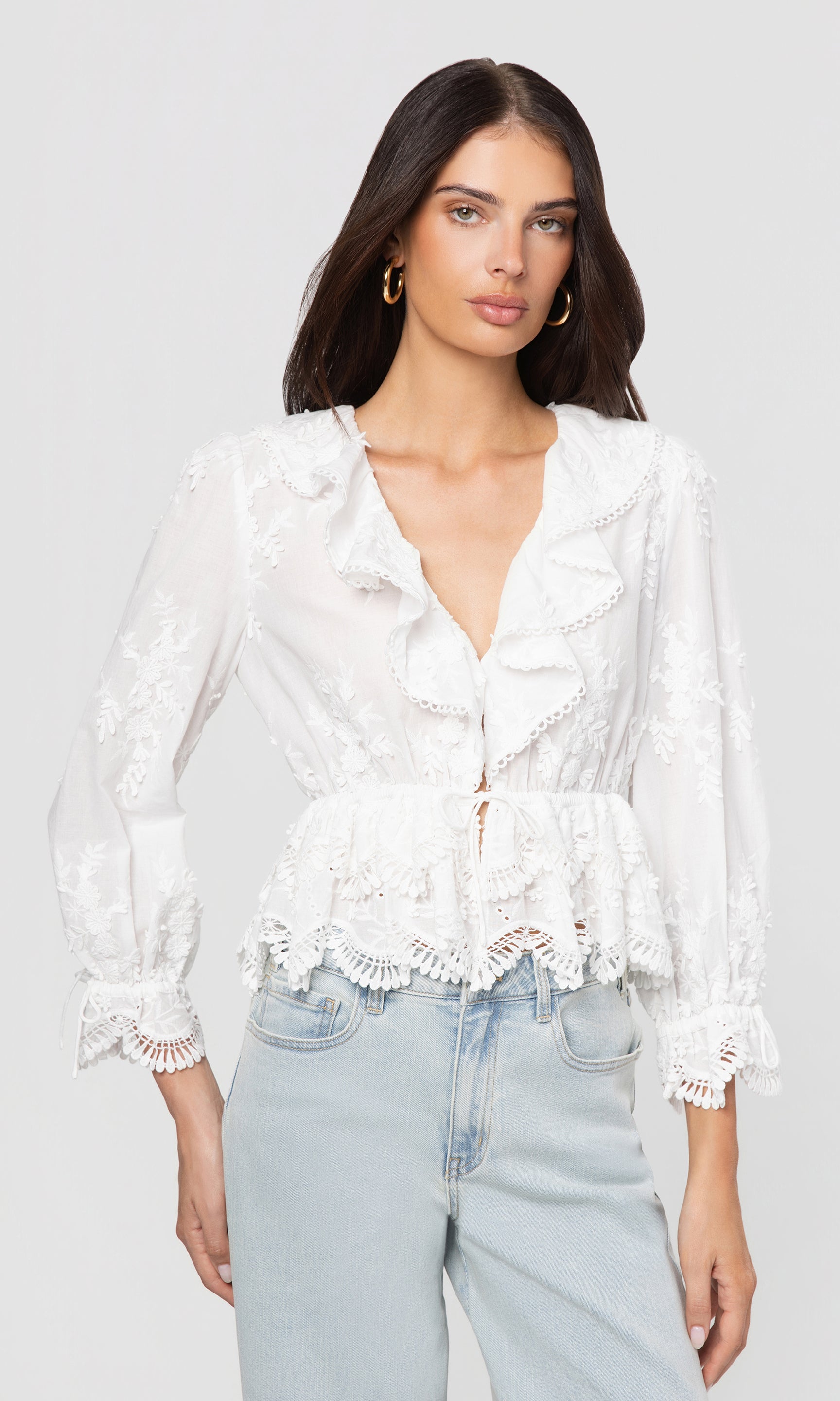 Woman wearing a white lace blouse and light blue jeans on a plain background