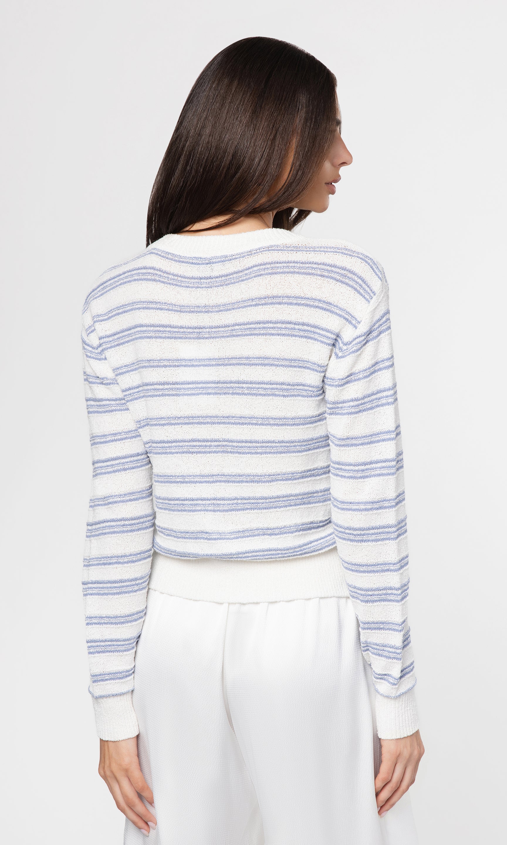 Back view of woman wearing a blue and white striped sweater against a plain background
