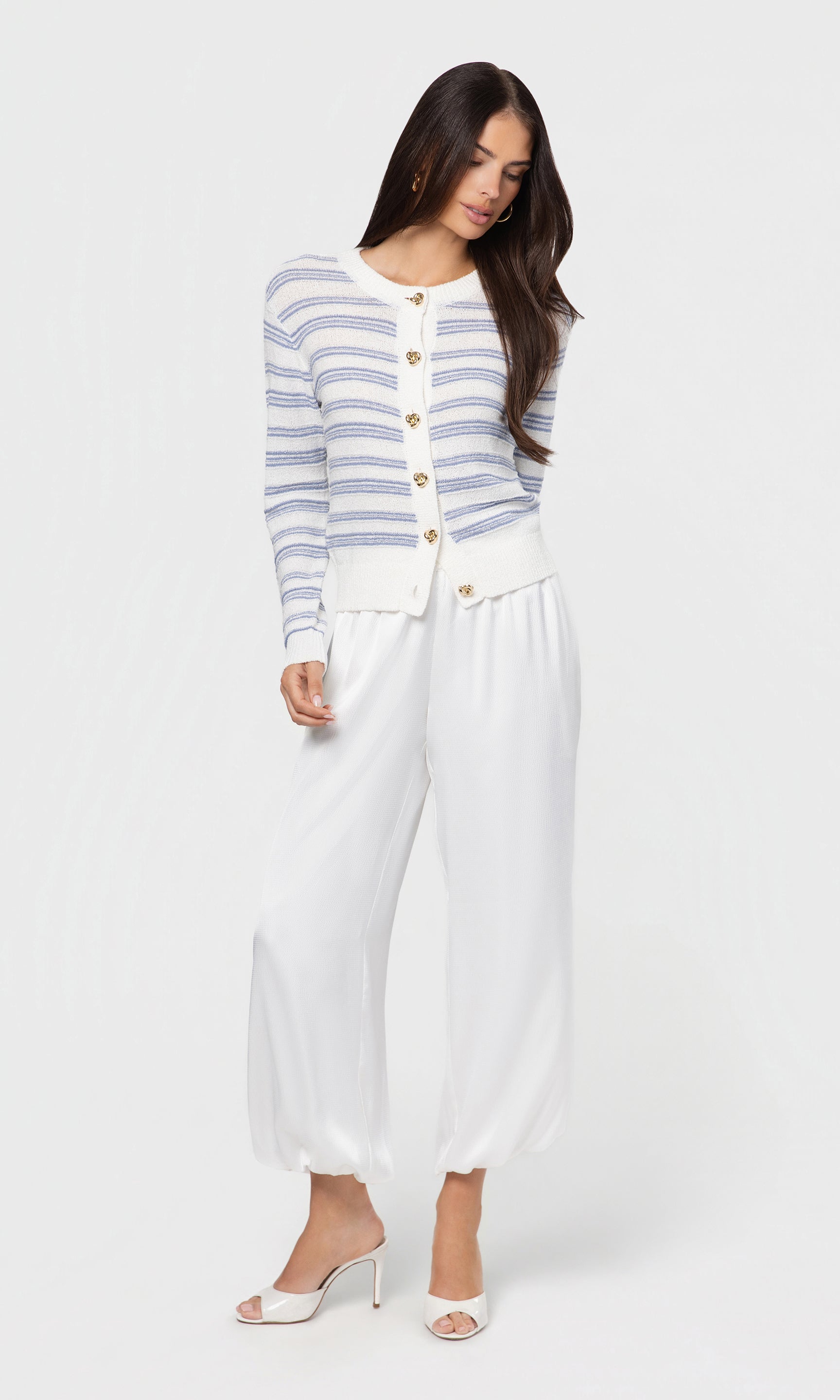 Woman wearing a striped cardigan and white pants on a white background