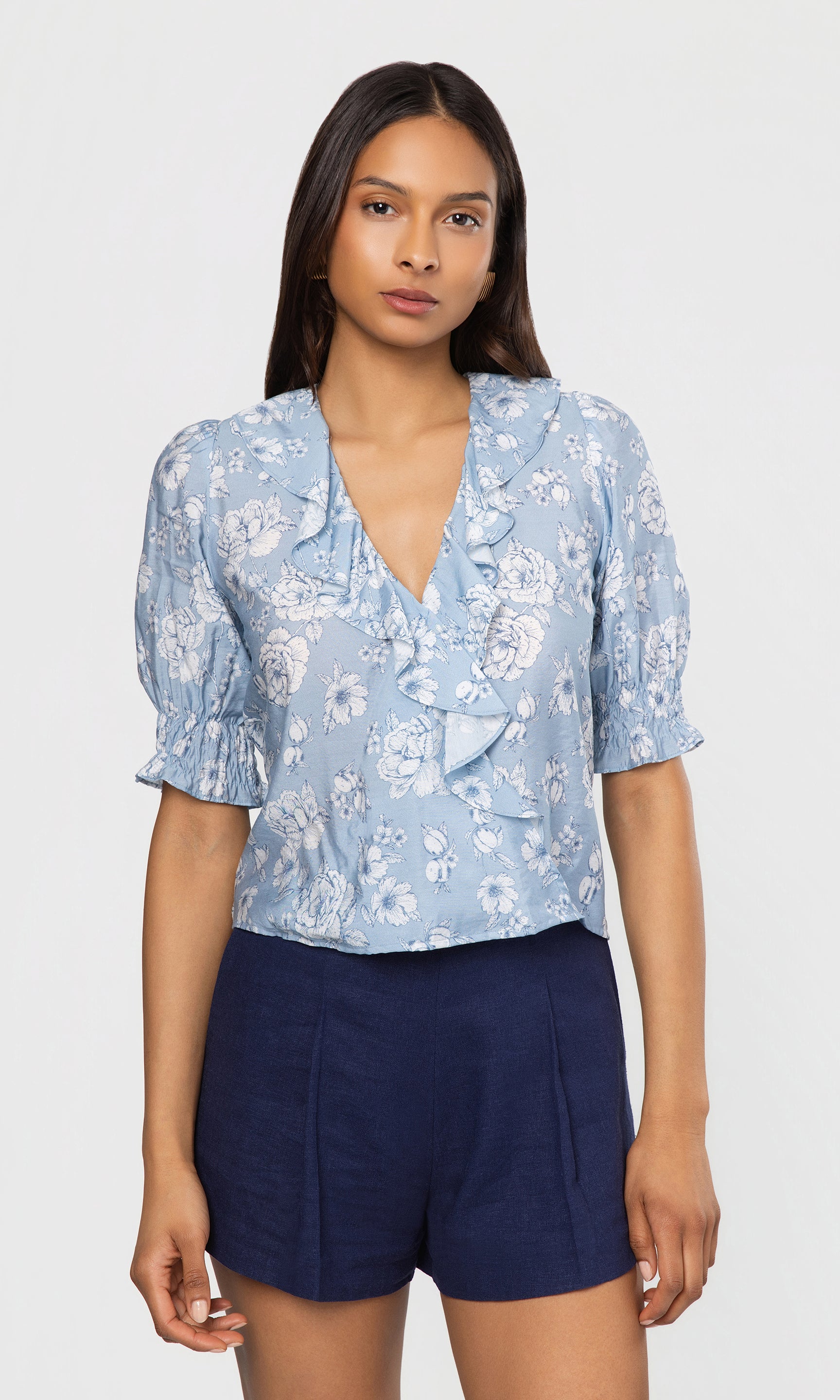 Woman wearing a light blue floral blouse and navy shorts on a white background