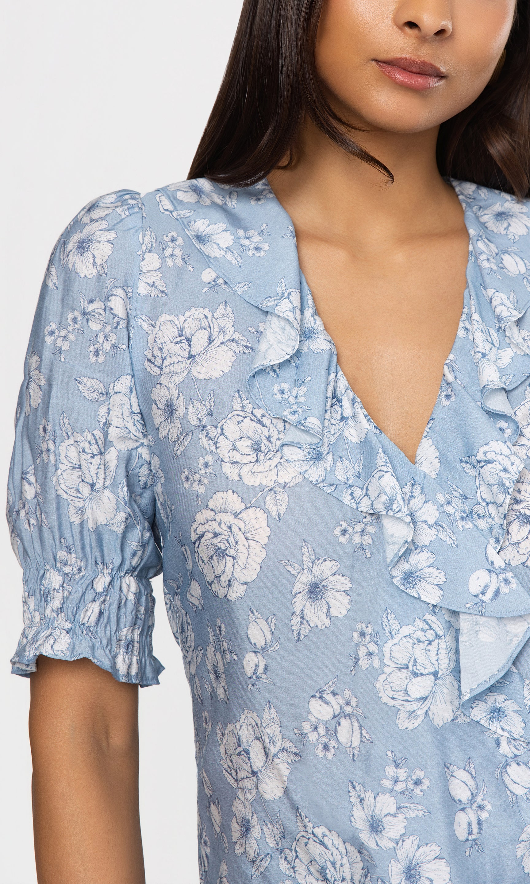 Close-up of woman wearing a blue floral blouse with a plain background