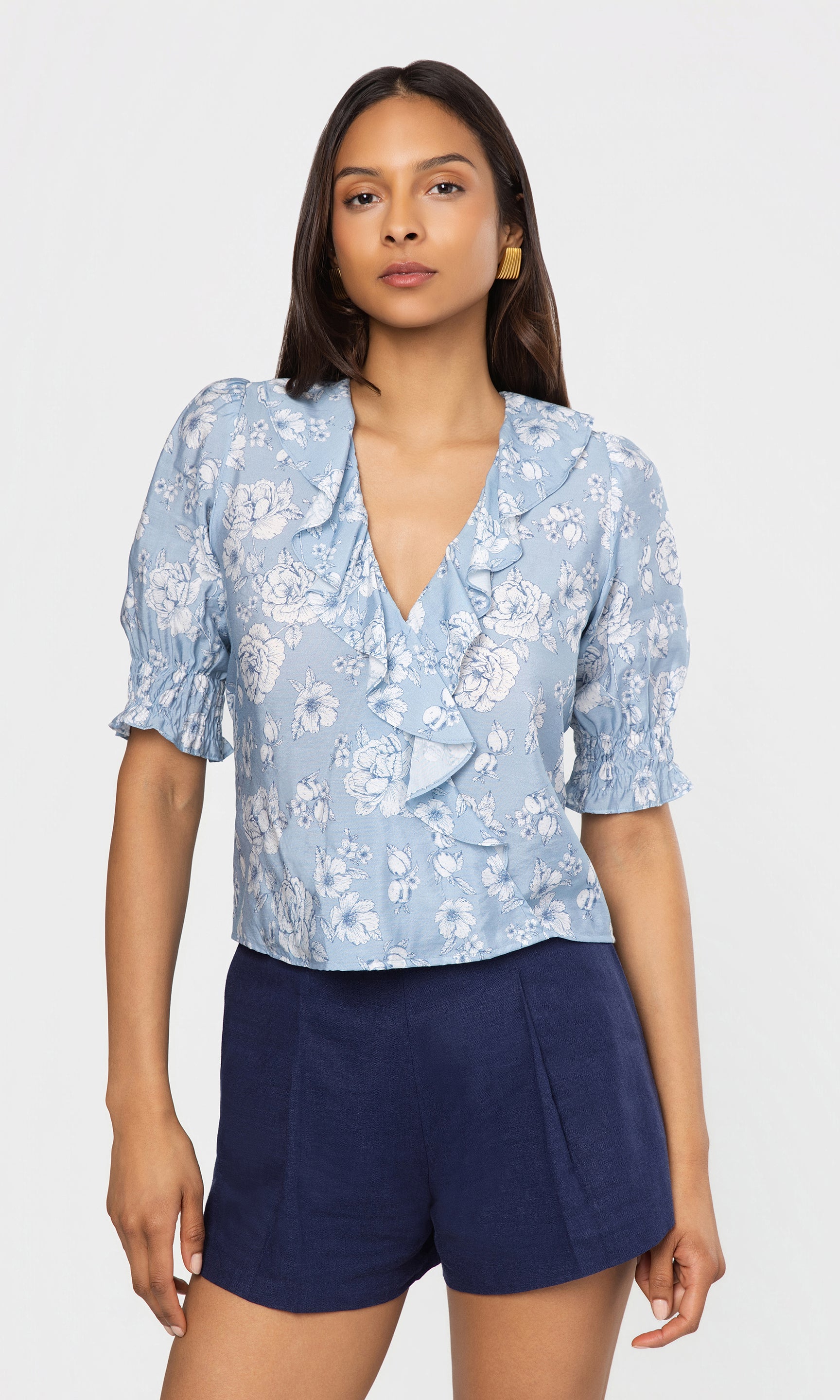 Woman wearing a light blue floral blouse and navy shorts on a white background
