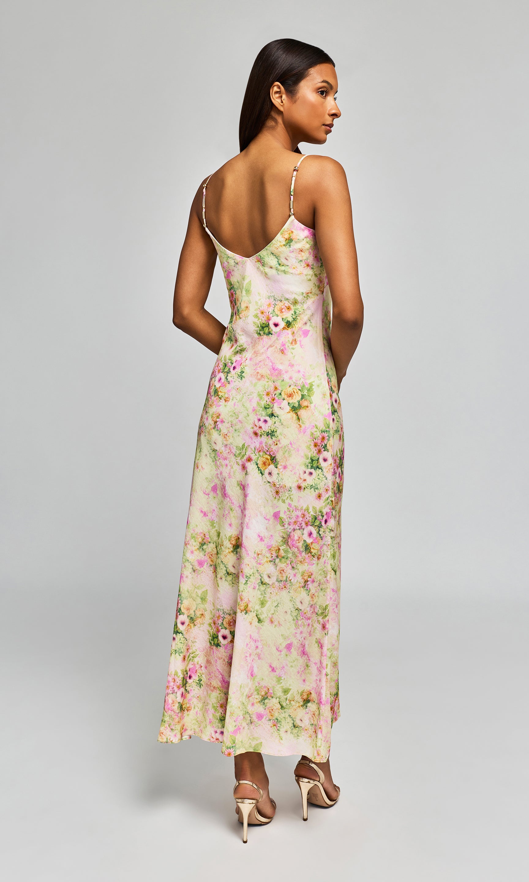 Back view of woman wearing a floral dress on a plain background.