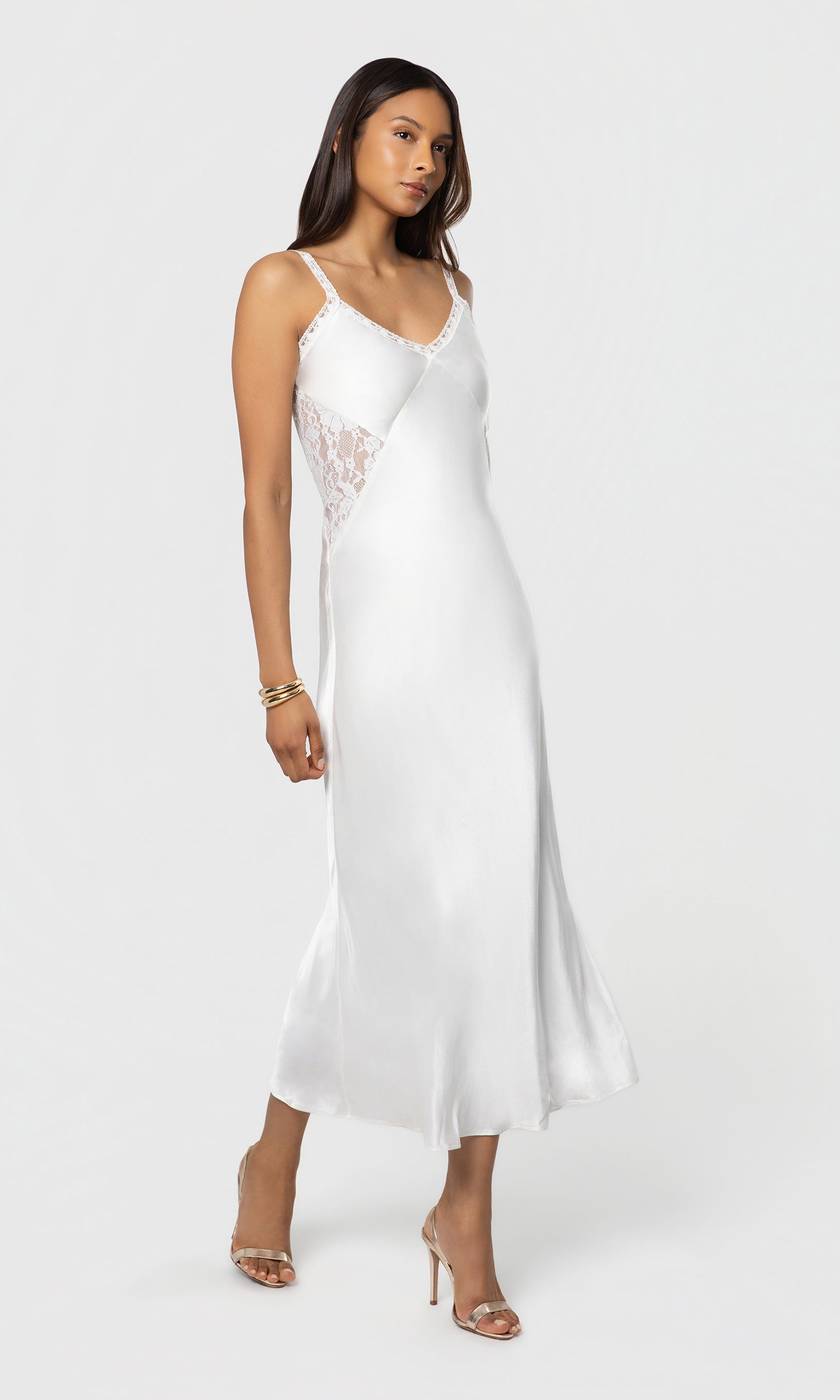 Side view of woman wearing a white slip dress with lace details on a white background