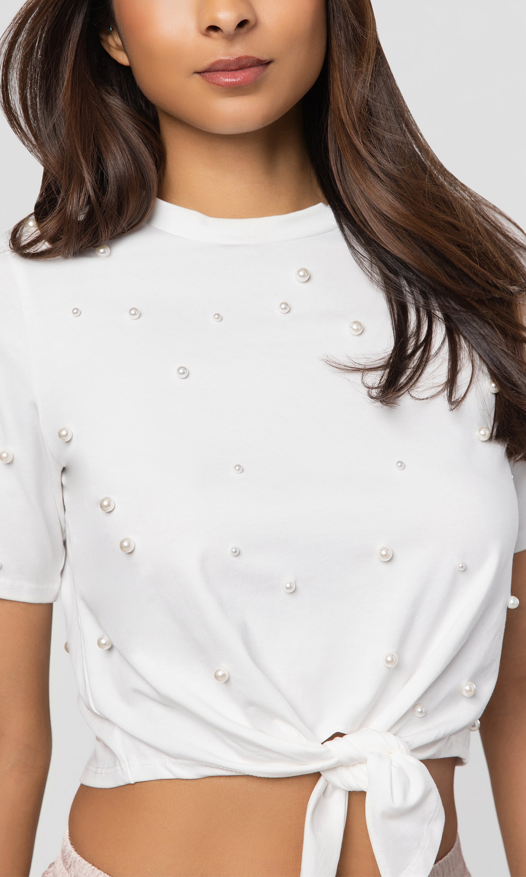Close-up of white top with pearl embellishments worn by a model on a white background