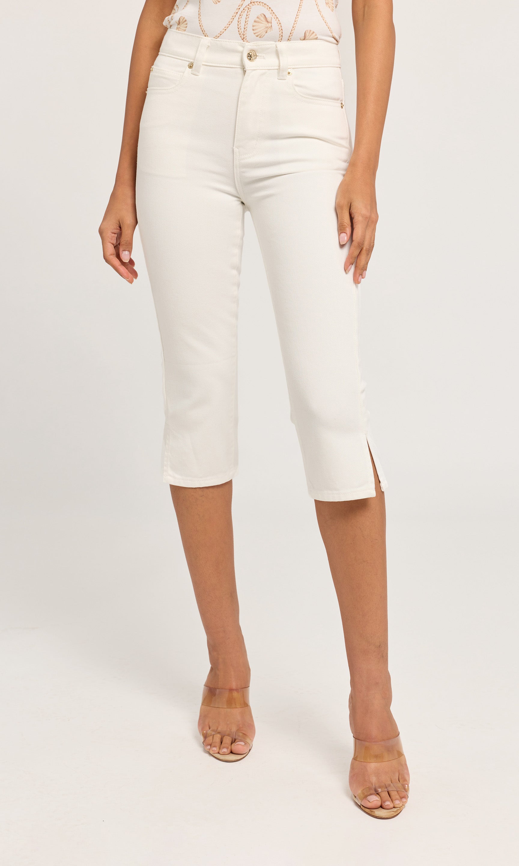 White capri jeans with side slits, shown on a model wearing clear high-heeled sandals.