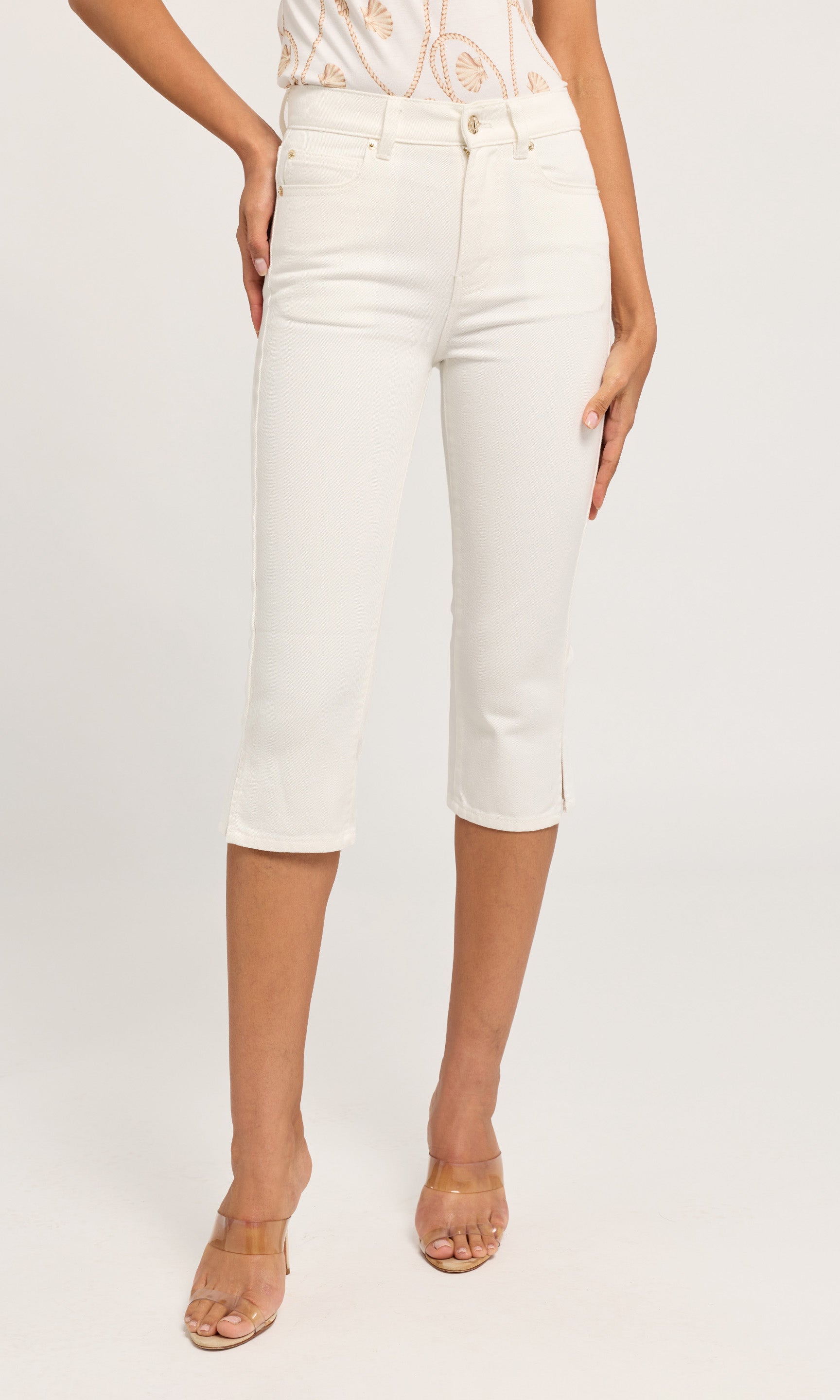White cropped capri jeans worn by a model, paired with a patterned top and clear-strap high-heeled sandals.