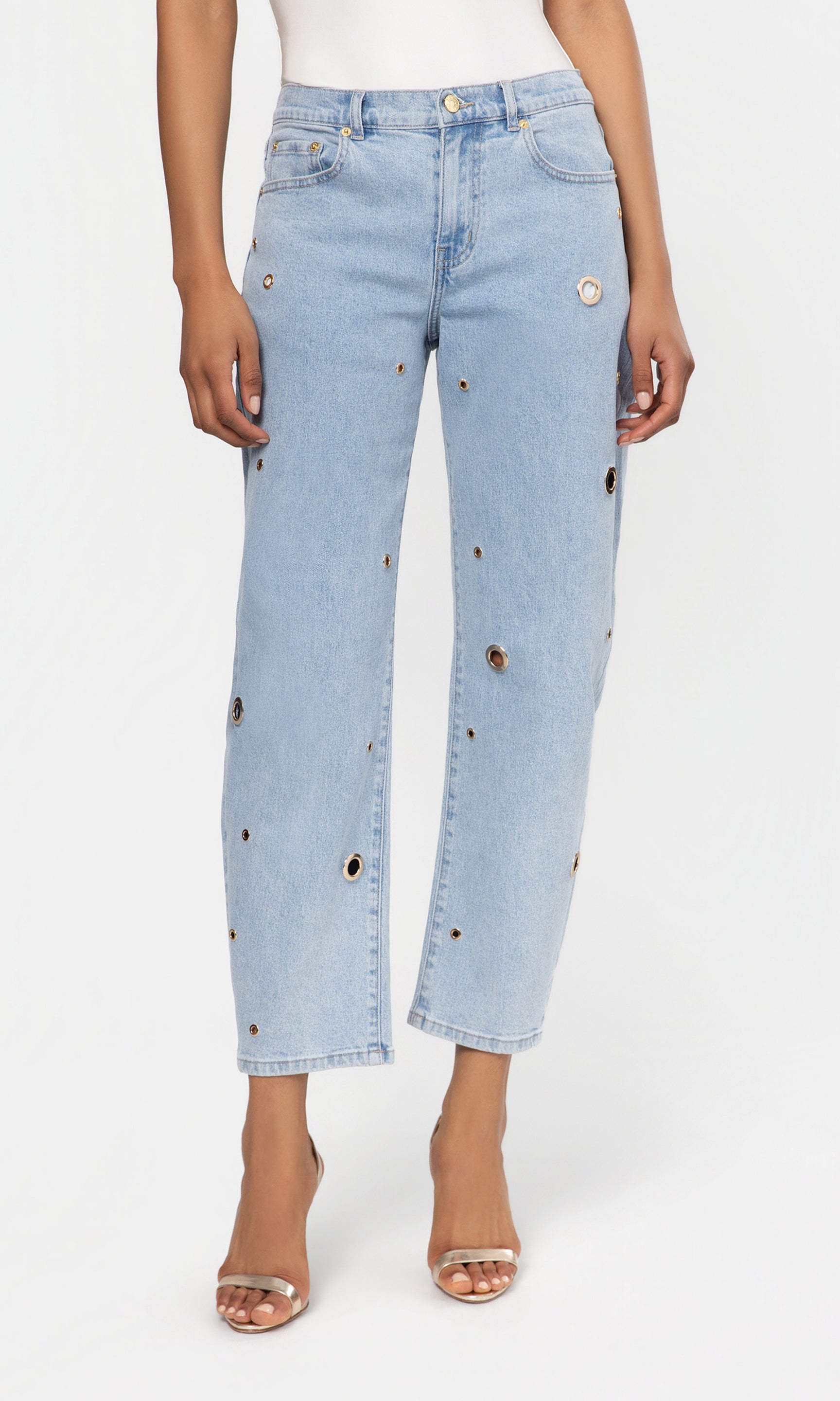 Light blue jeans with decorative grommets worn by a person on a white background