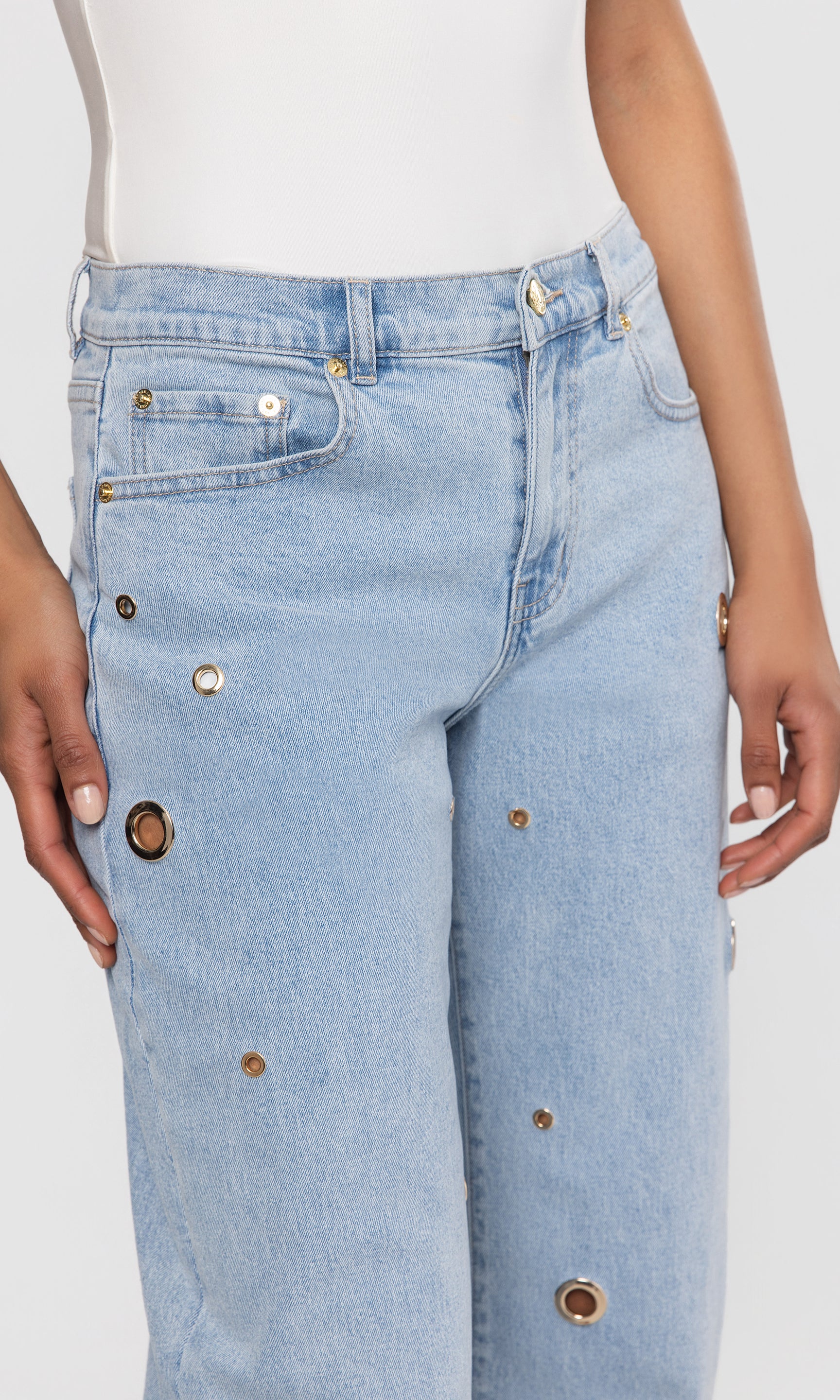 Close-up of light blue jeans with grommet details on a white background