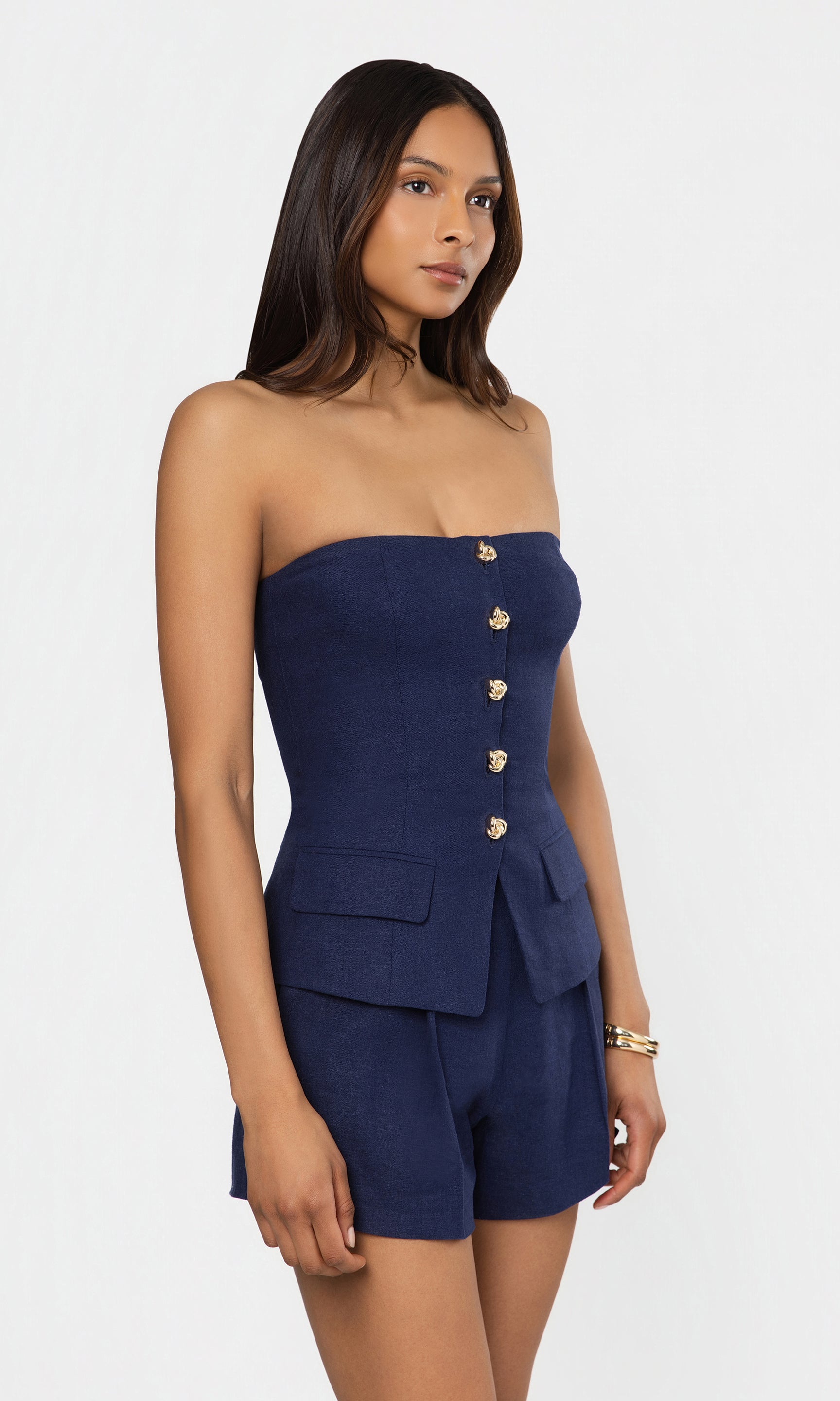 Side view of woman wearing a strapless navy blue outfit with gold buttons on a white background