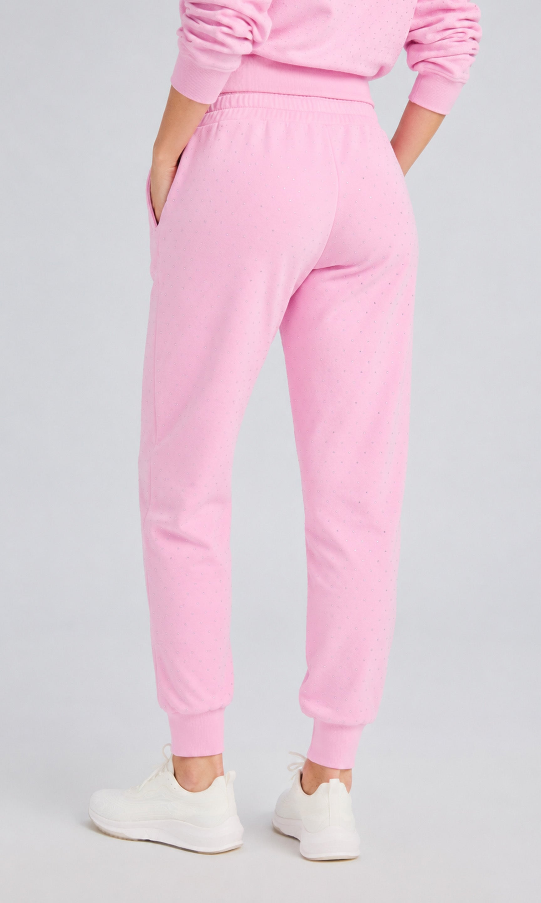 Back view of model wearing poppy pink pants with crystal embellishments and a matching sweater on a plain background.