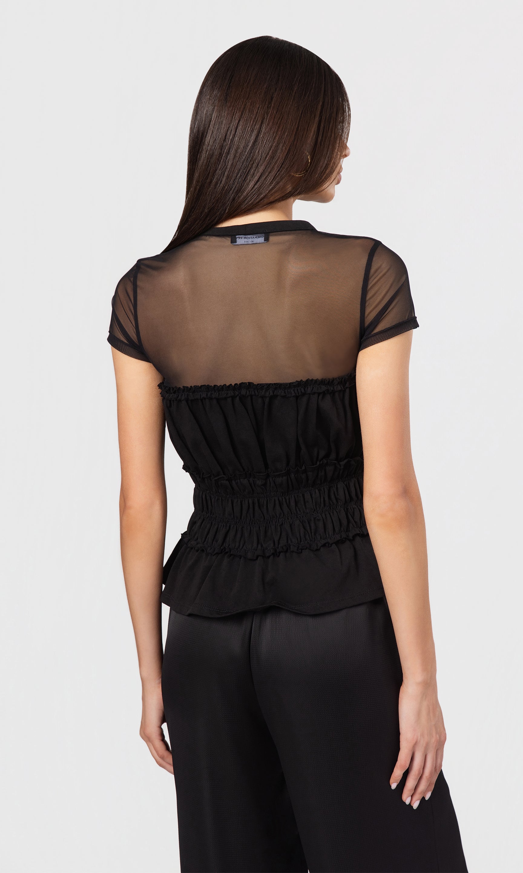 Back view black sheer top with ruffled details worn by a model on a white background