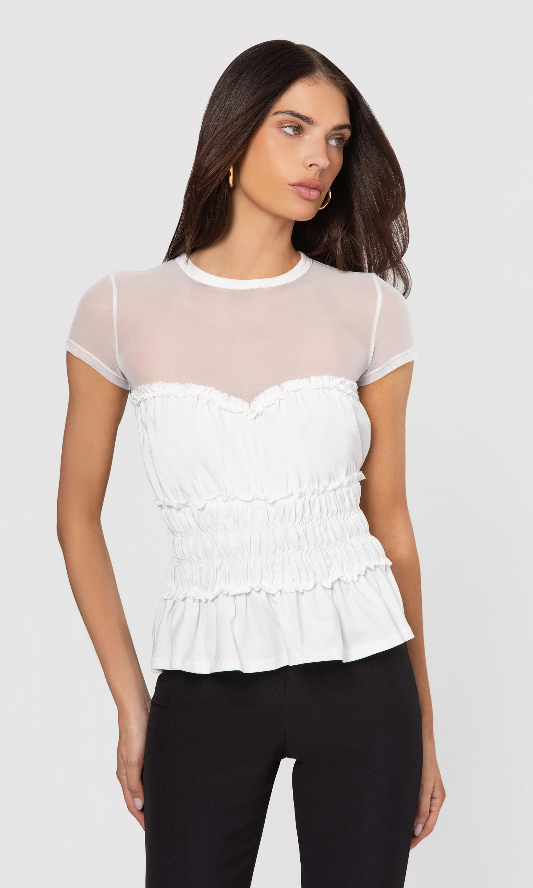 Woman wearing a white peplum top with sheer sleeves on a plain background