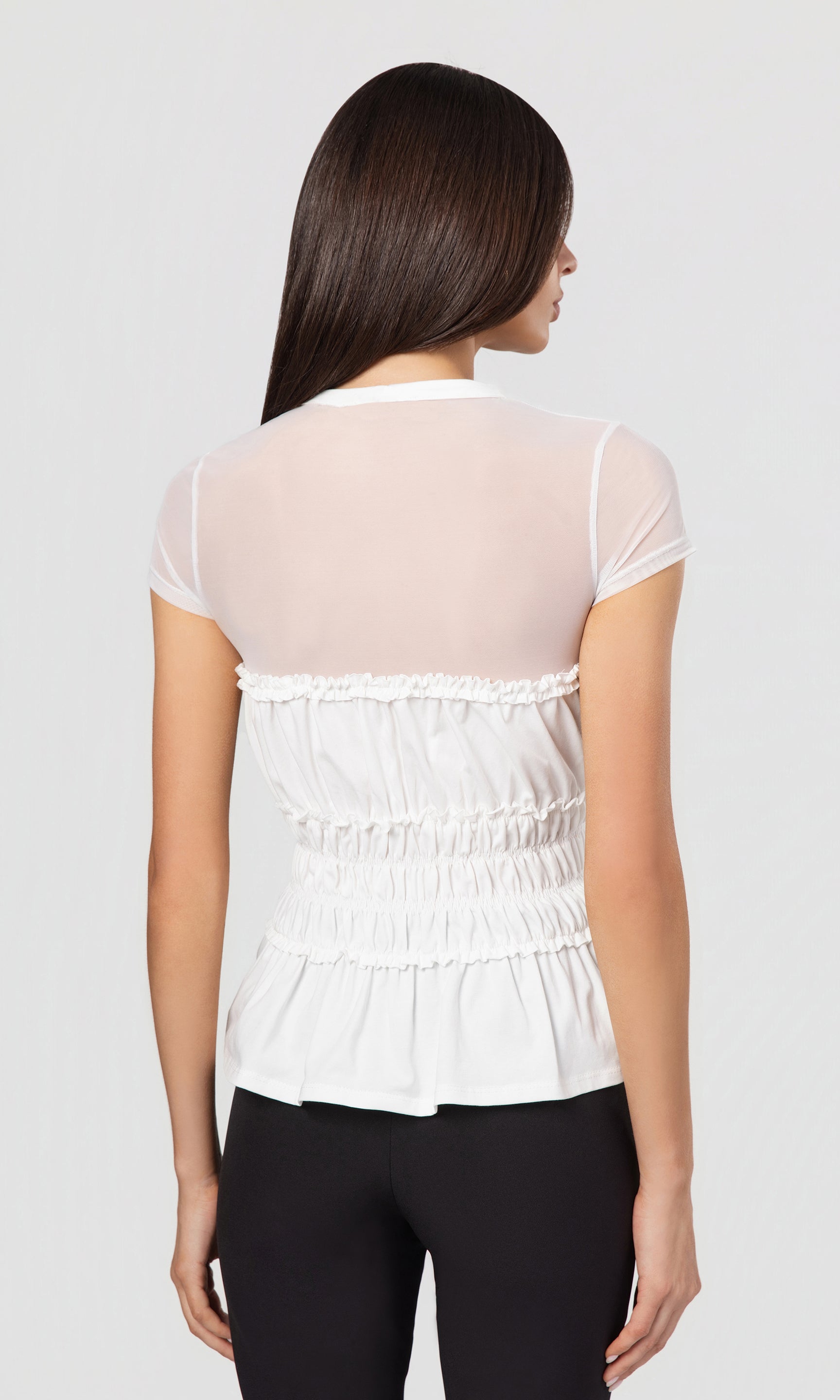 Back view of woman wearing a white blouse with sheer sleeves on a light gray background