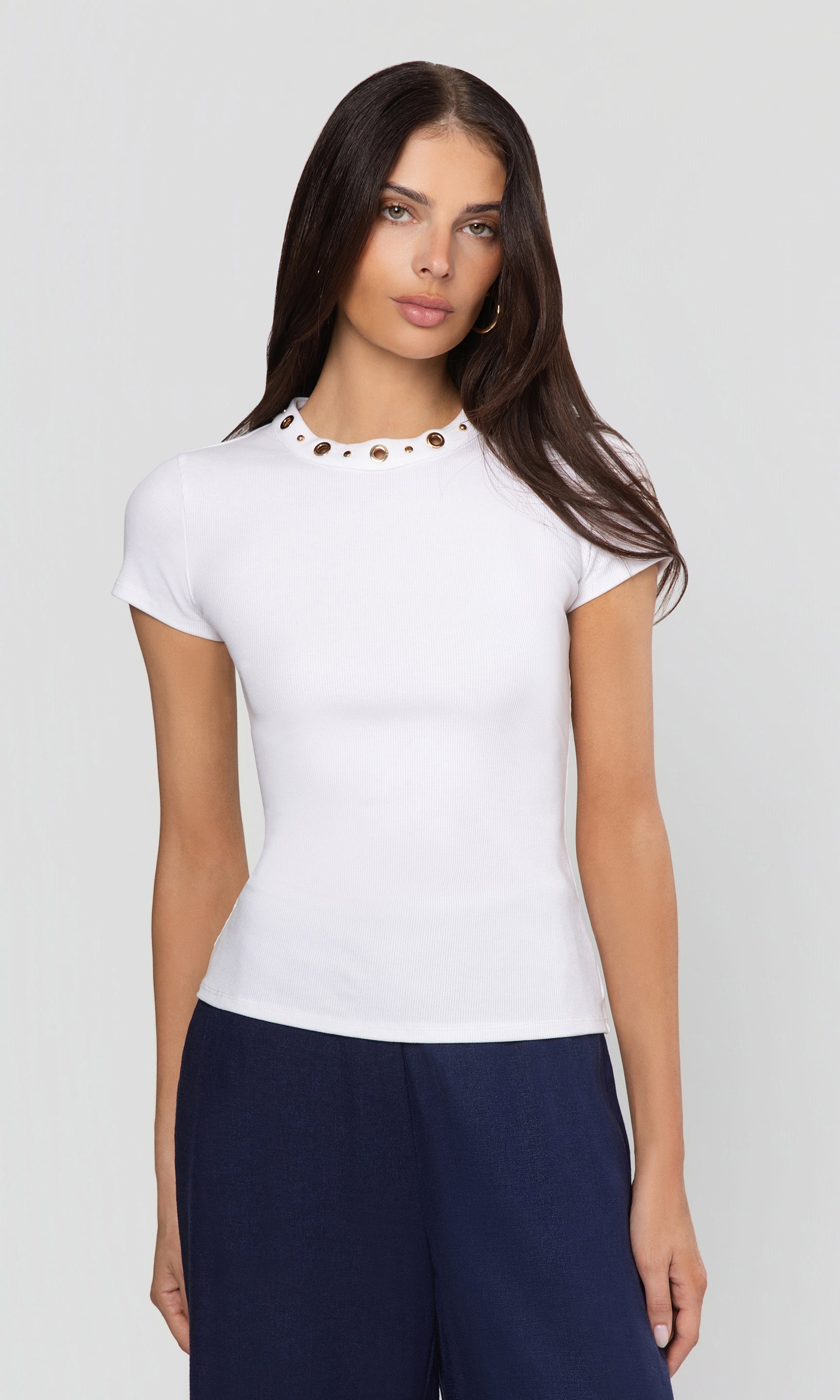 Woman wearing a white top with decorative elements on a plain background
