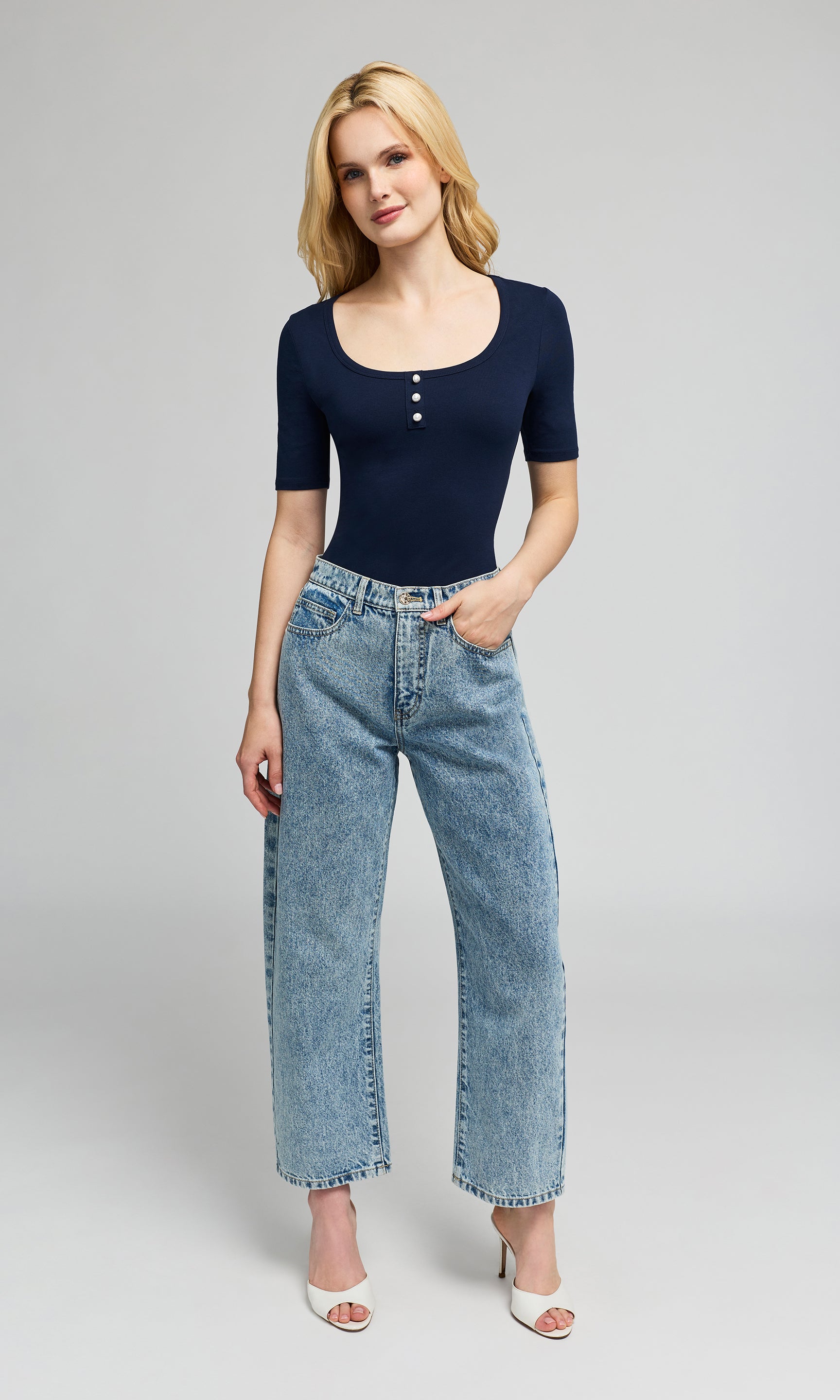 Woman wearing a navy blue top and light blue jeans on a gray background
