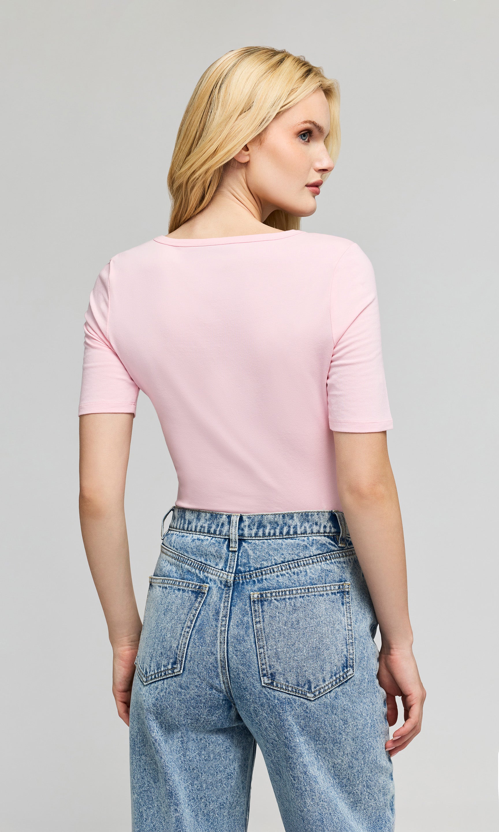 Back view of model wearing a light pink short-sleeve top paired with light-wash blue jeans.