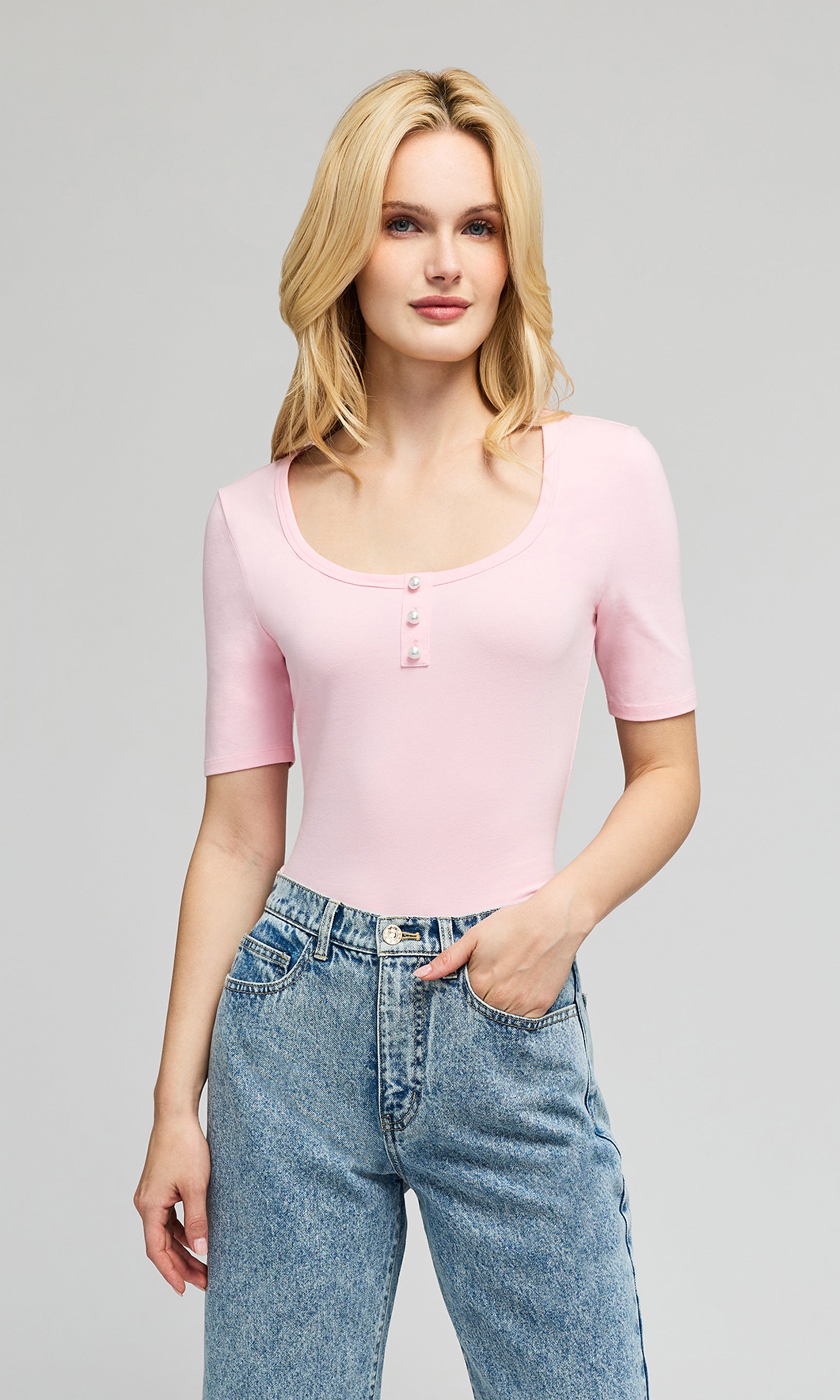 Model wearing a light pink short-sleeve top with pearl buttons on the chest, paired with light-wash blue jeans.