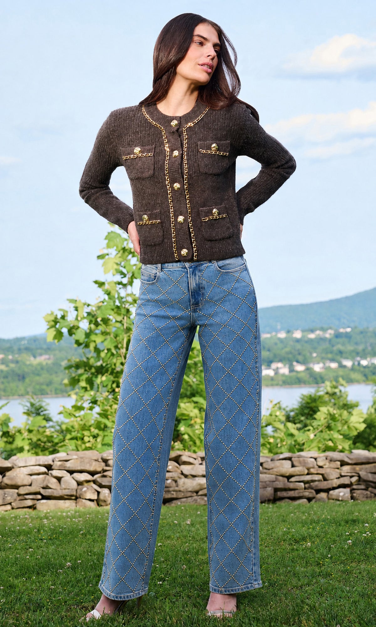 Model stands outdoors on grass wearing a brown textured cardigan with gold-tone buttons, paired with light blue jeans featuring a subtle geometric pattern.