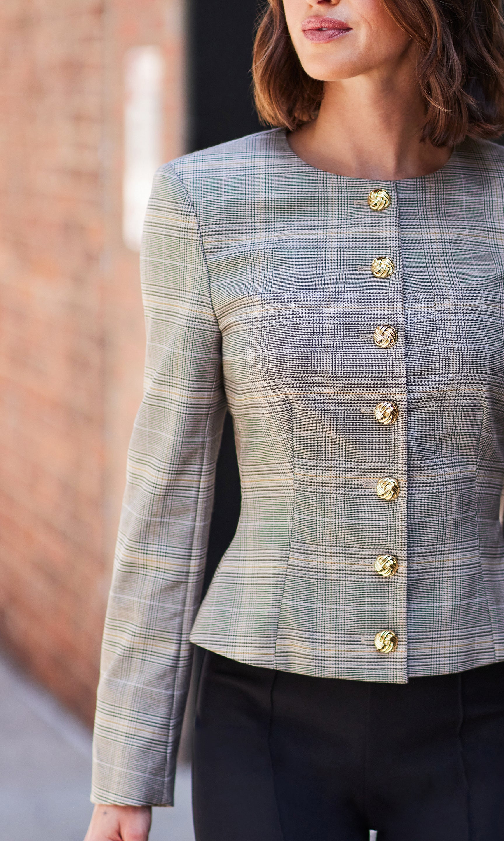 Front view of the Sirus Plaid Jacket styled with black pants, photographed against a brick wall.