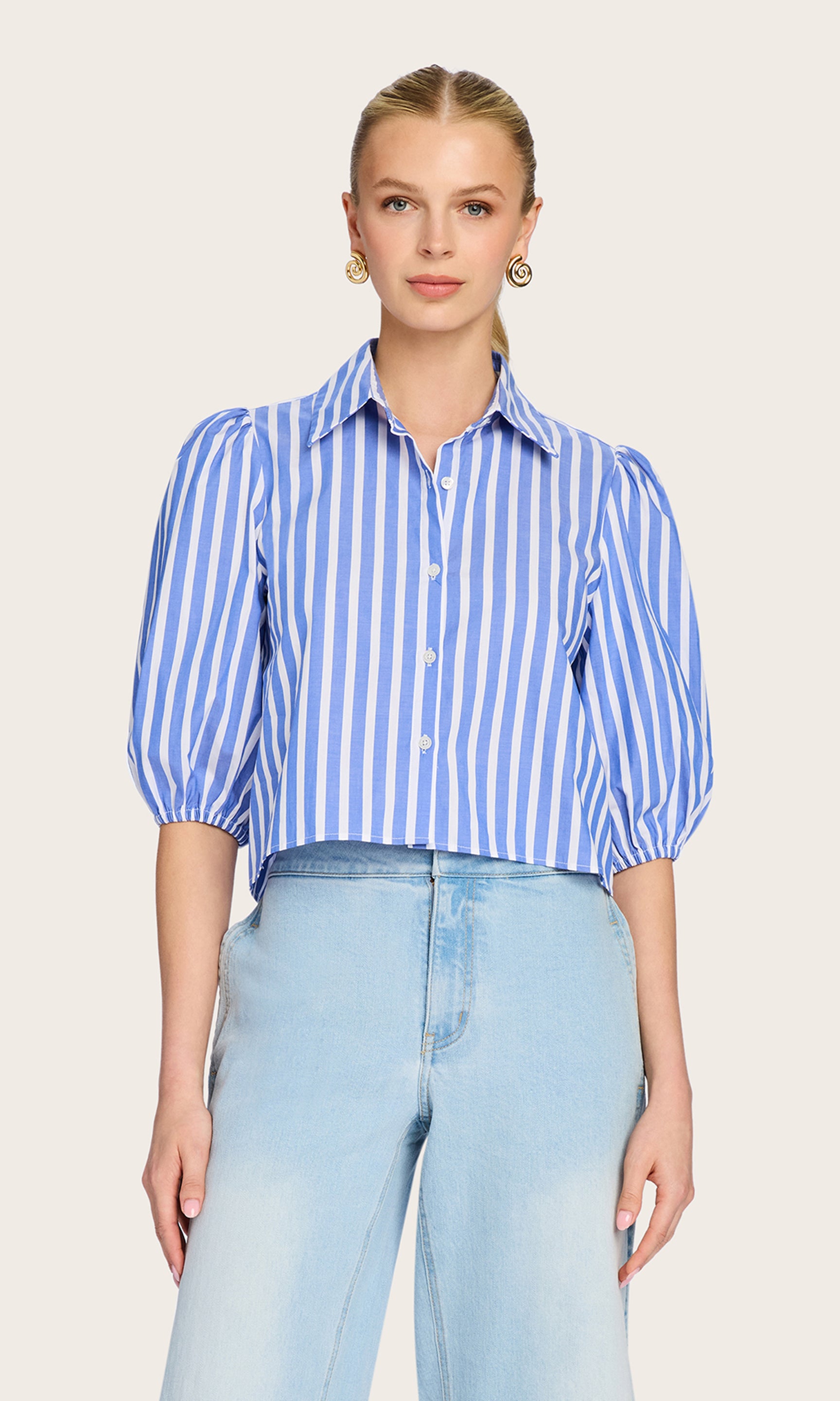Front view image of model wearing the Tammy Stripe Shirt in white/blue paired with blue jeans and gold earrings.