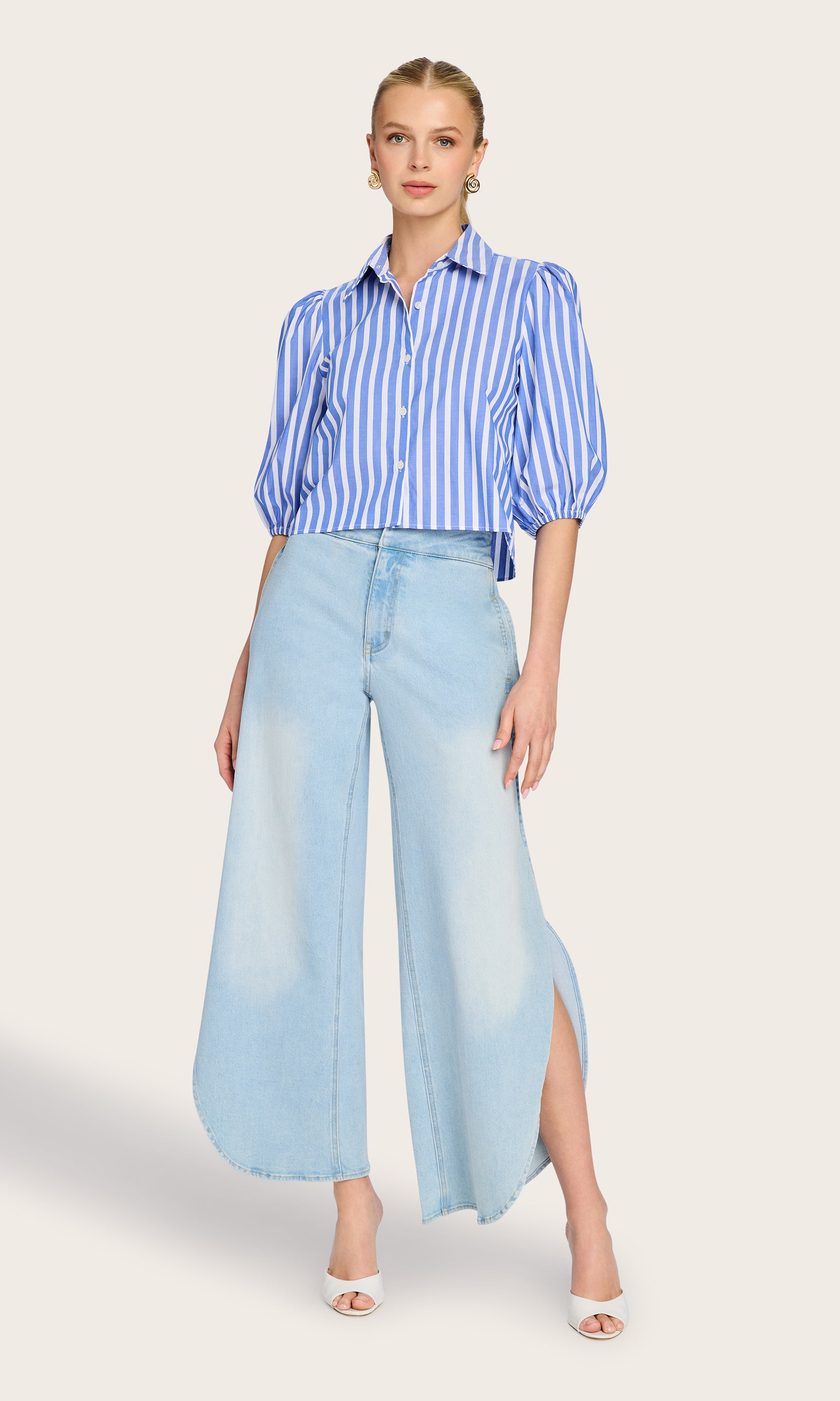 Full body image of model wearing the Tammy Stripe Shirt in white/blue paired with blue jeans, white heels and gold earrings.