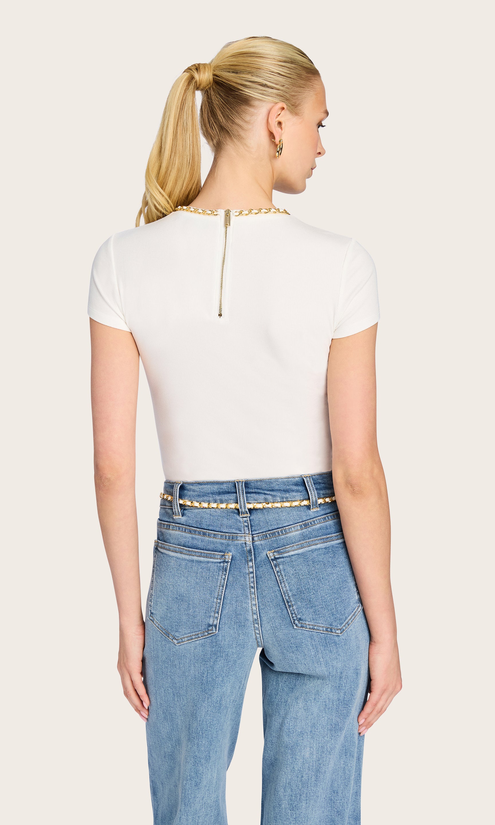back image of model wearing the Tate t-shirt in white with a chain detail on the neckline and a zipper down the top to mid back, paired with blue jeans