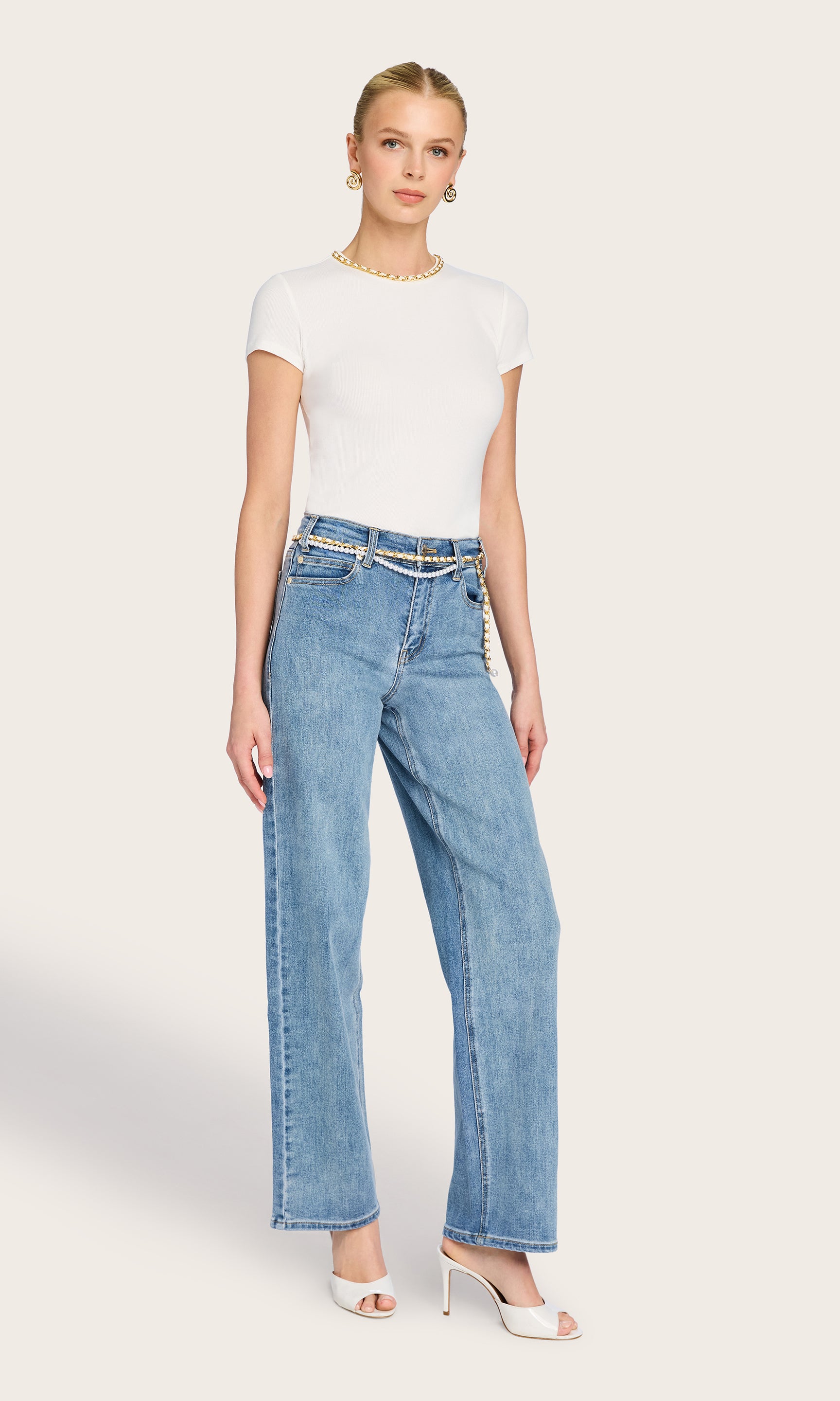full body image of model wearing the Tate t-shirt in white with a chain detail on the neckline, paired with blue jeans and white heels