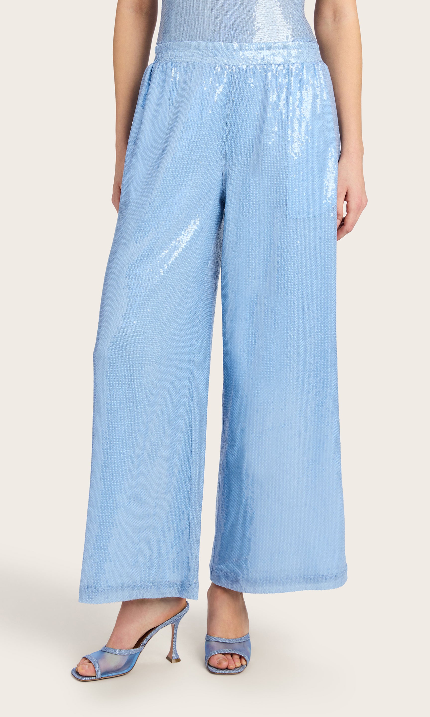 Front view image of the model wearing the Talia Sequin Pants in light blue, styled with a matching sleeveless bodysuit and heels.