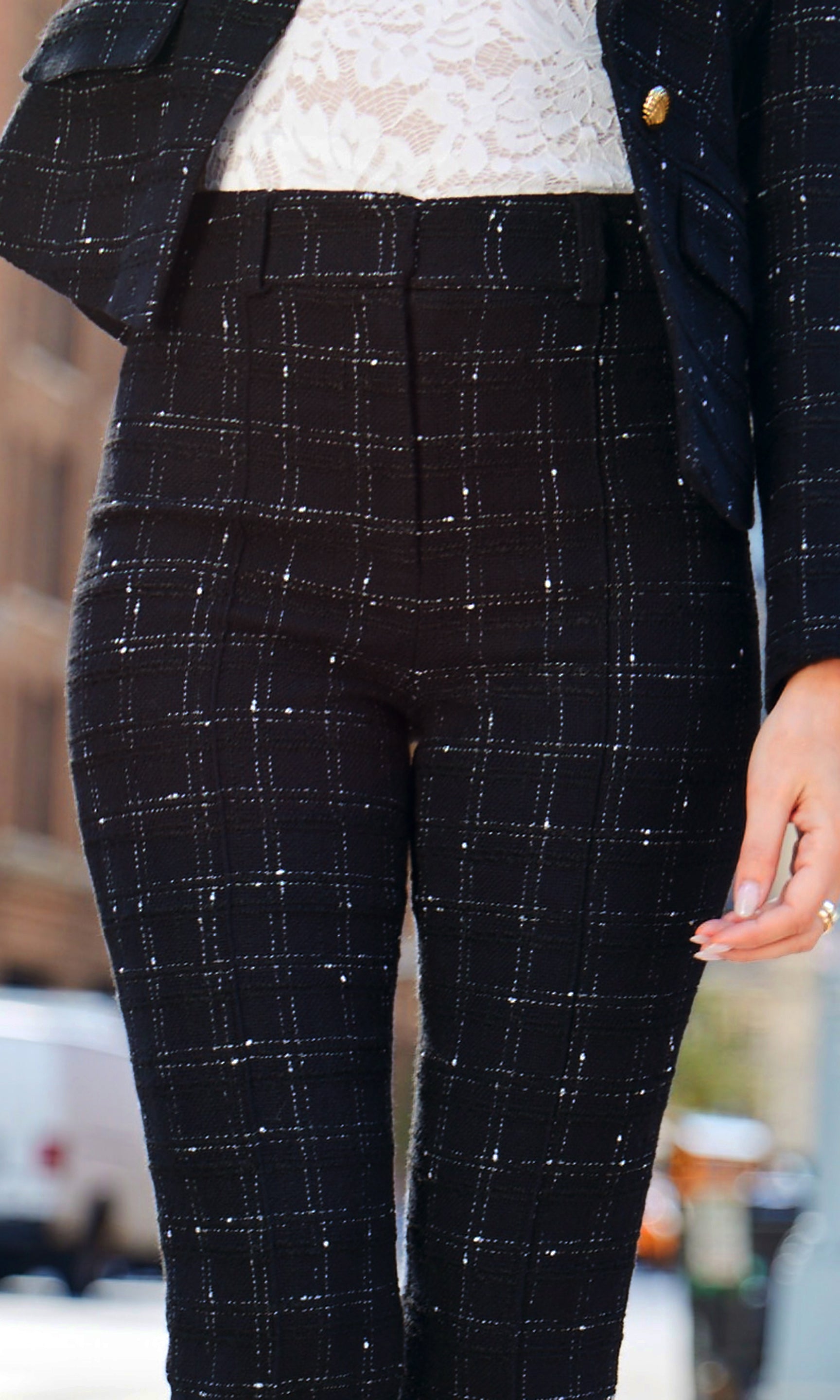 Close-up of black plaid pants worn with matching blazer and white lace top, blurred background