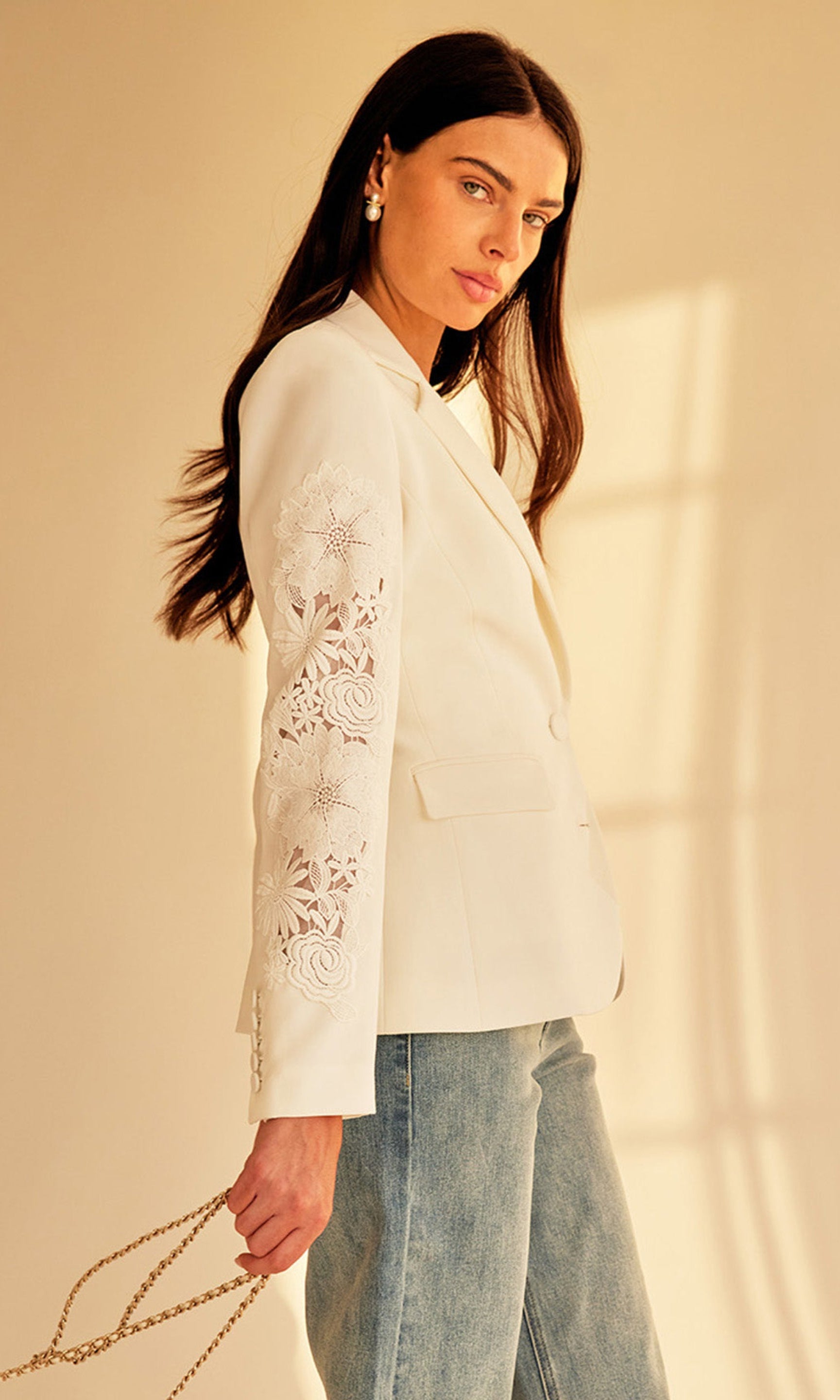 Indoor shot of the model wearing the Venturi Lace Combo Blazer with denim, holding a gold bag for a casual-luxe look.
