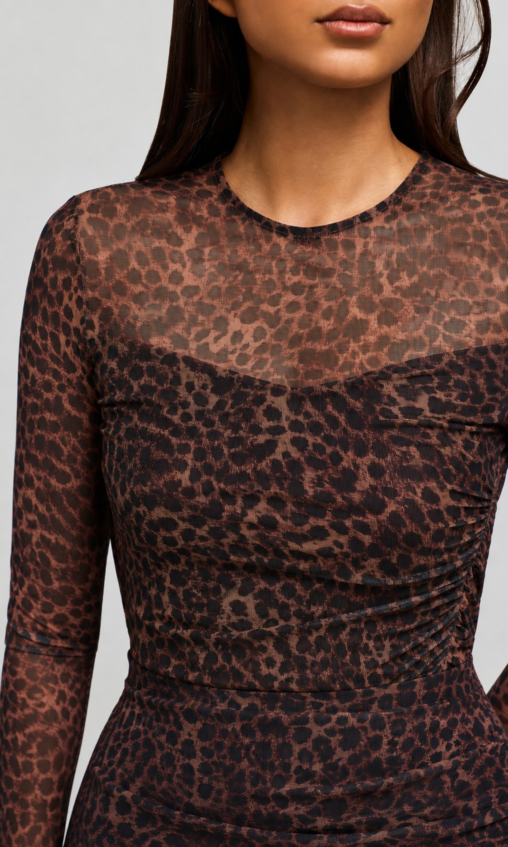 A close-up of a model wearing a sheer leopard-print long-sleeve top with a gathered sweetheart neckline and ruched bodice.