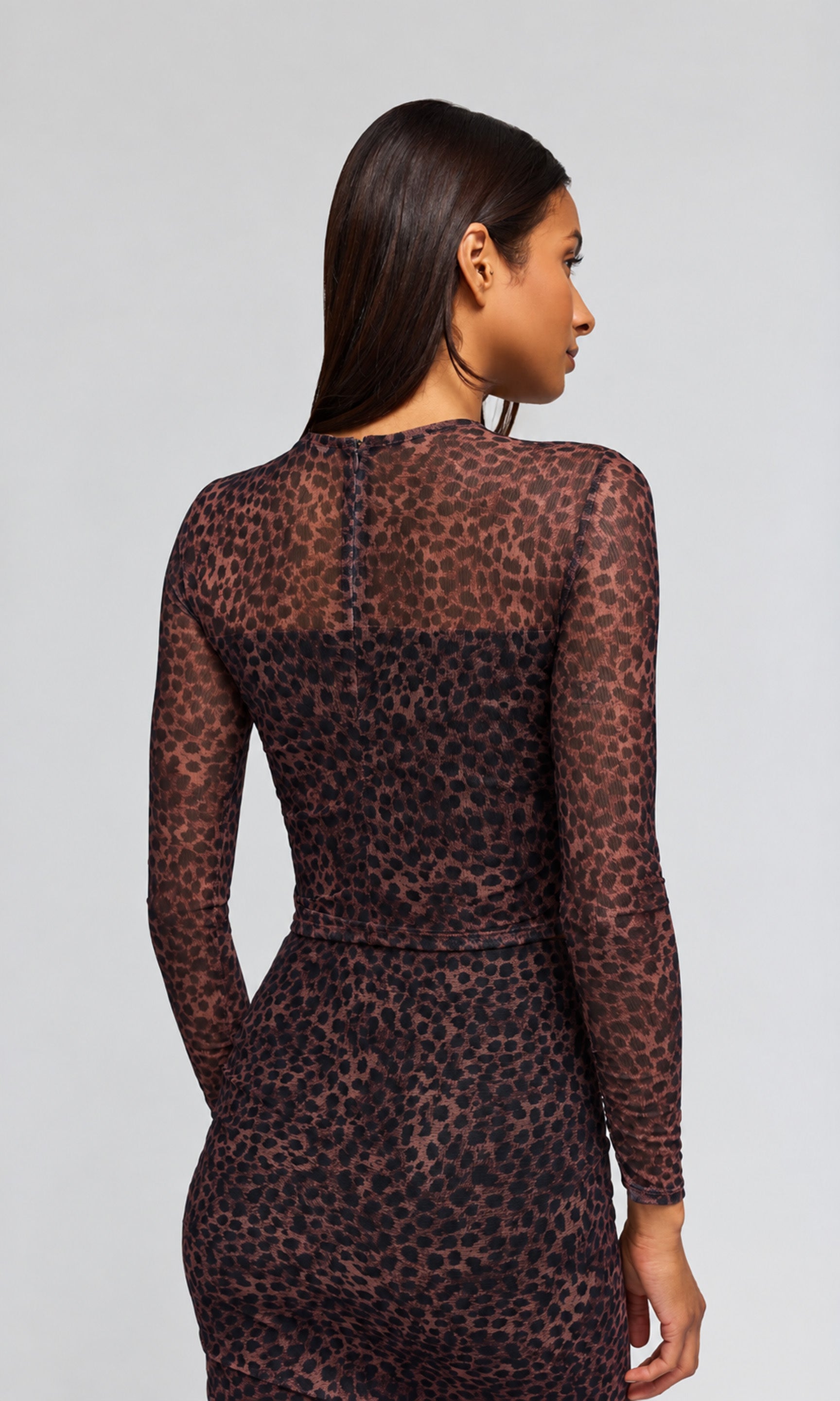 Back view of a woman modeling a sheer long-sleeve mesh top and matching skirt with a dark brown and black leopard print.