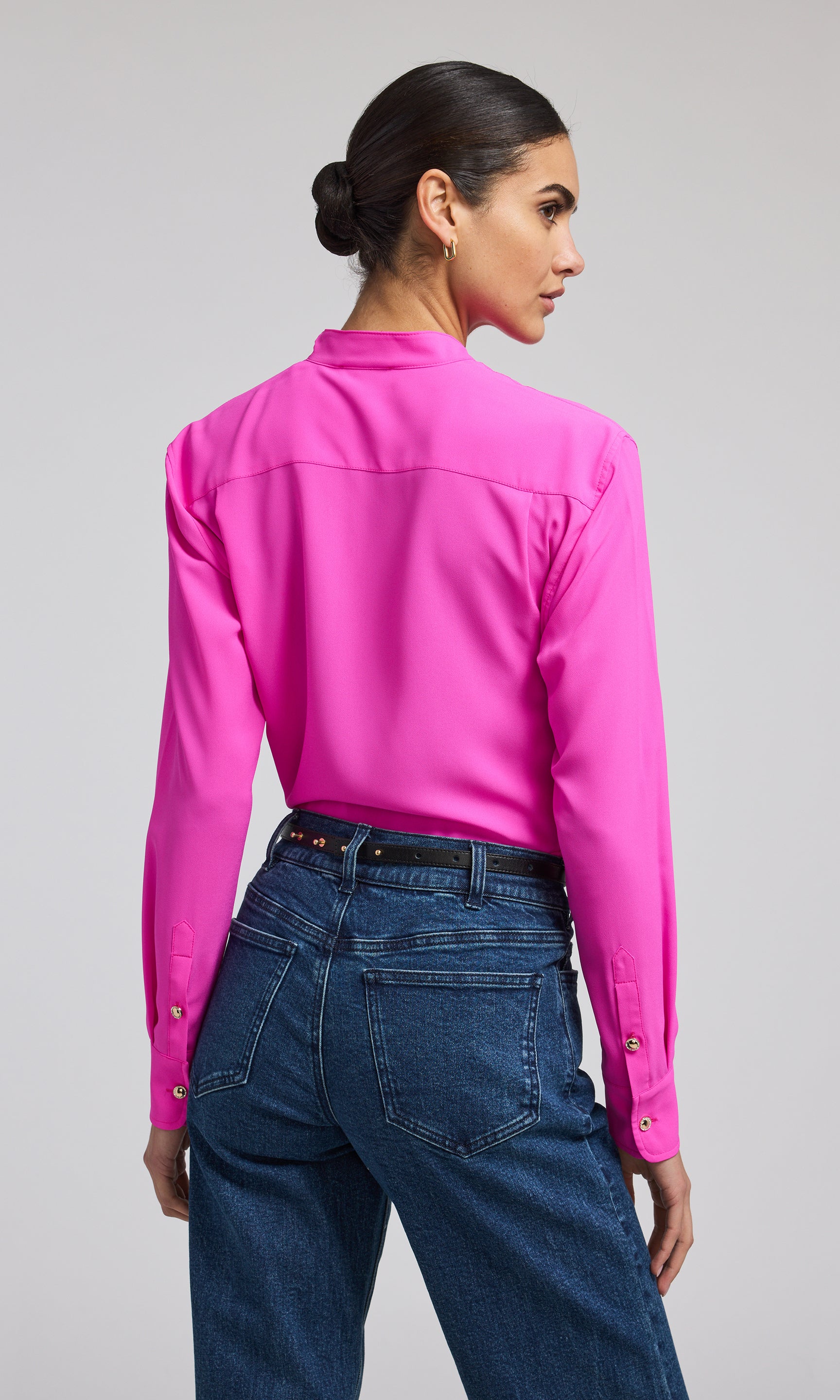 A model showcases a stylish hot pink blouse with gold buttons, highlighting its elegant design and sophisticated color.