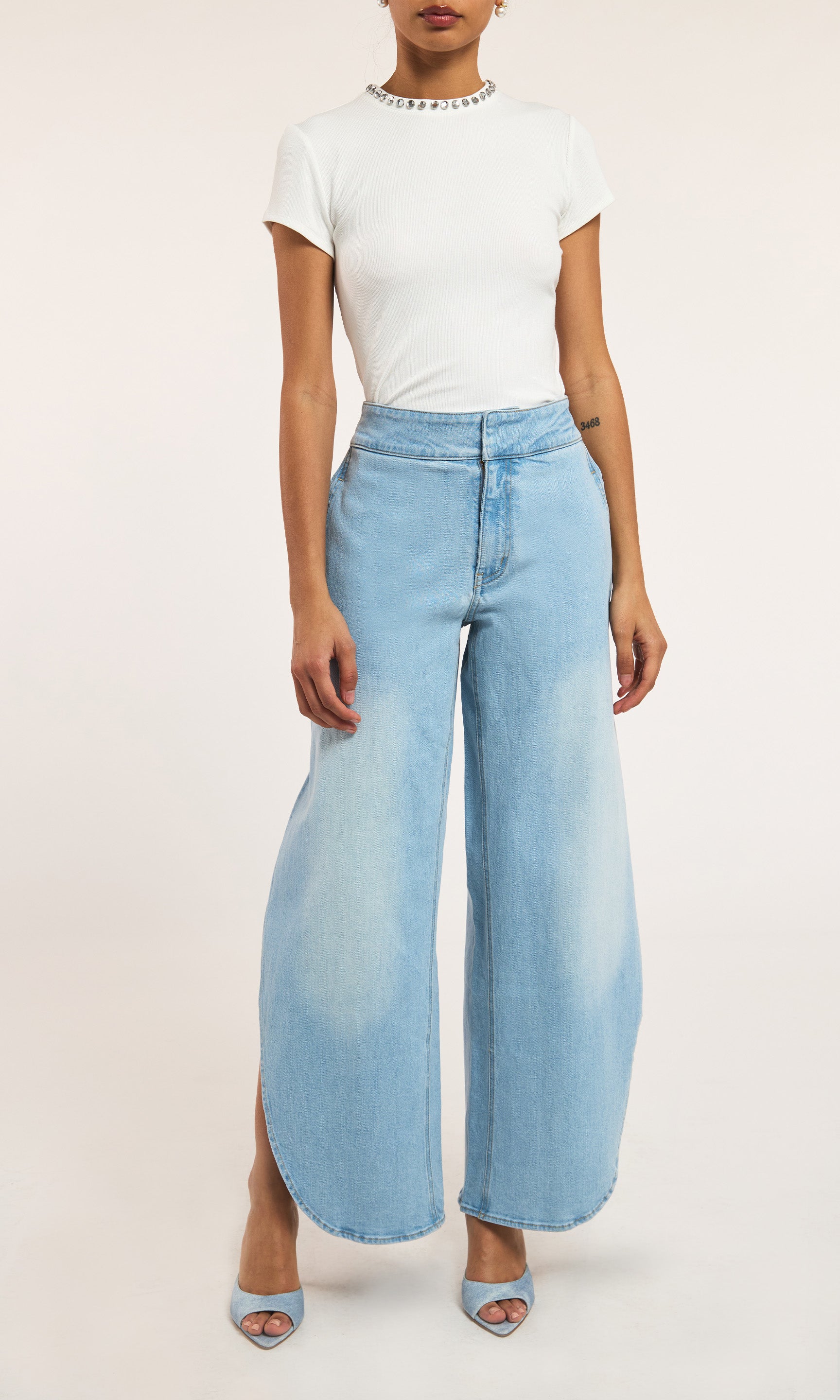 Model wearing a white top and light blue wide-leg jeans on a plain background
