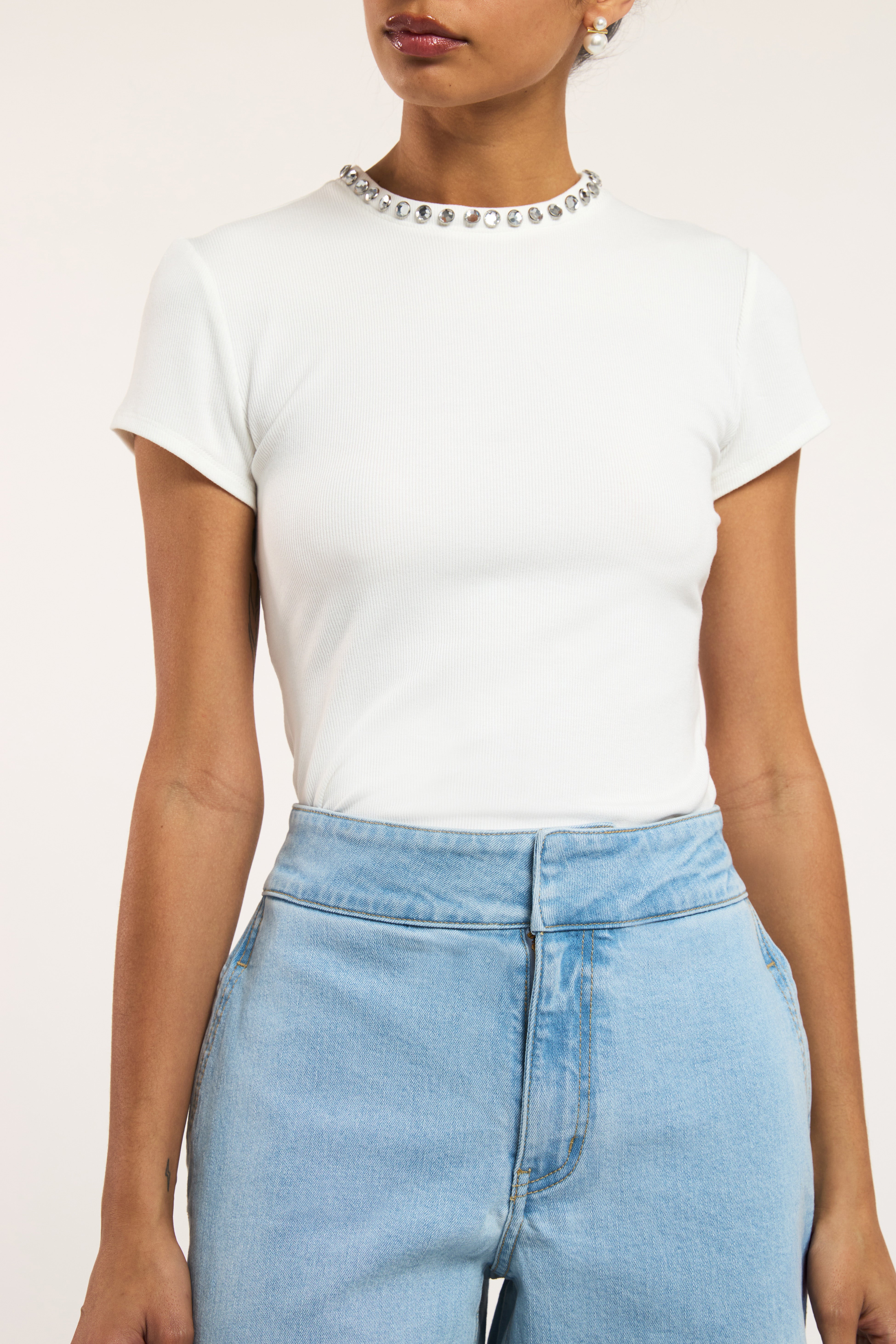 Model stands wearing a white tee shirt with crystal embellished neckline