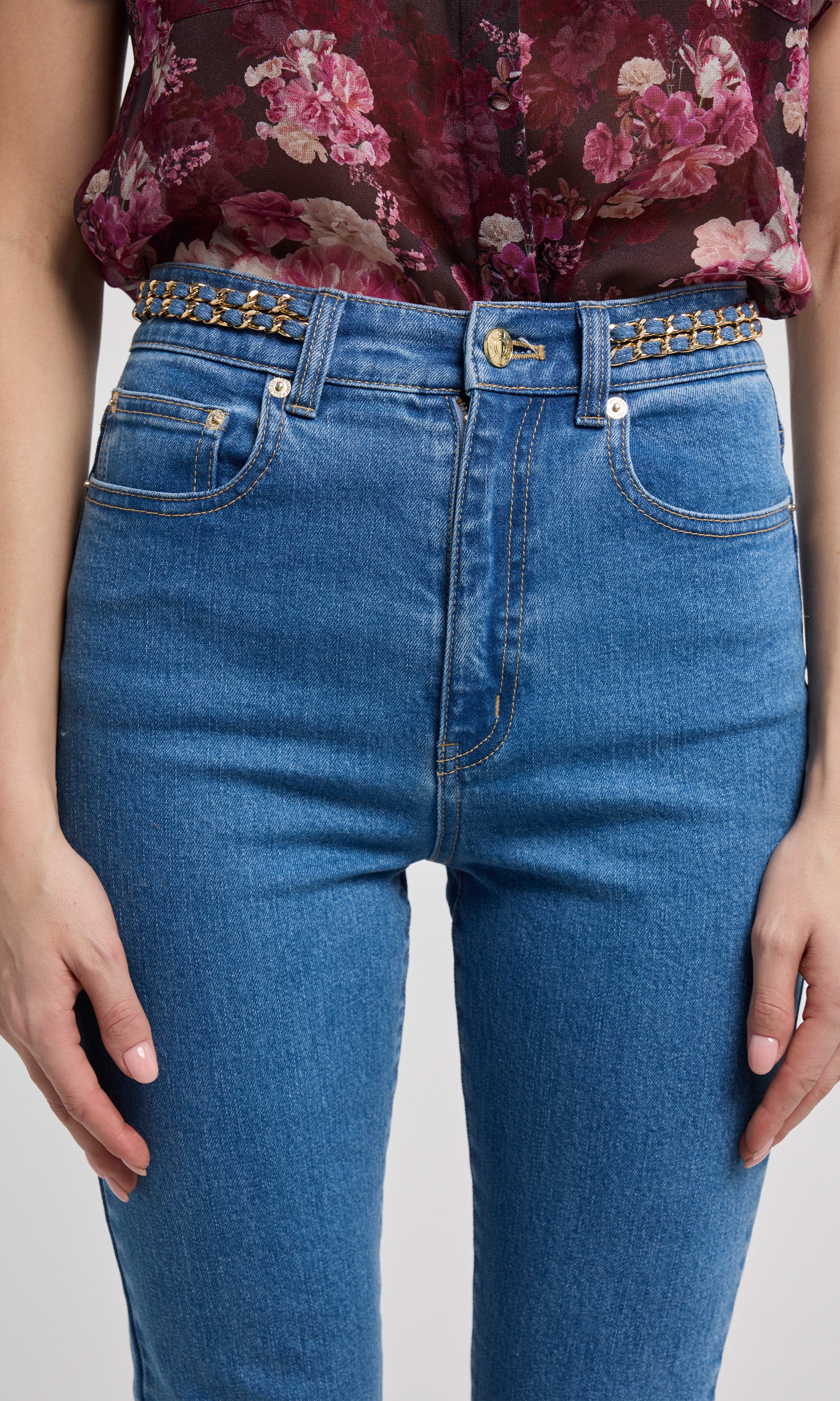 Person wearing blue jeans with a floral top on a white background