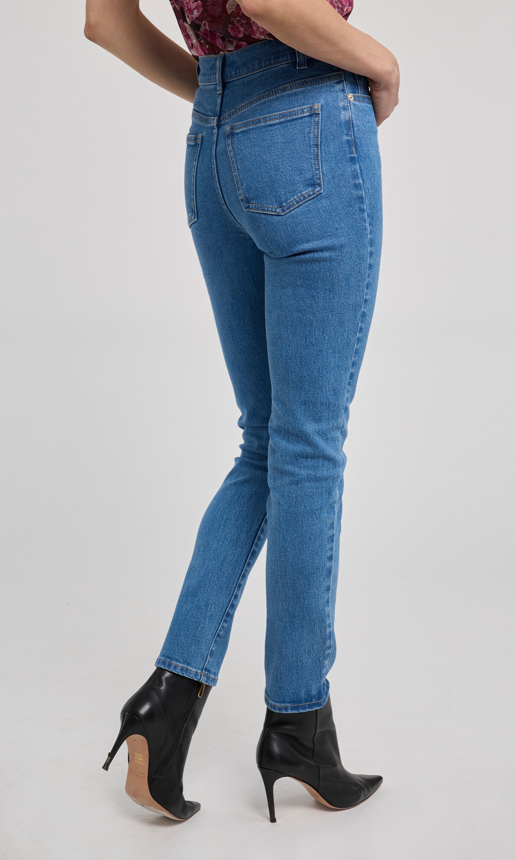 Person wearing blue jeans and black high-heeled shoes on a white background