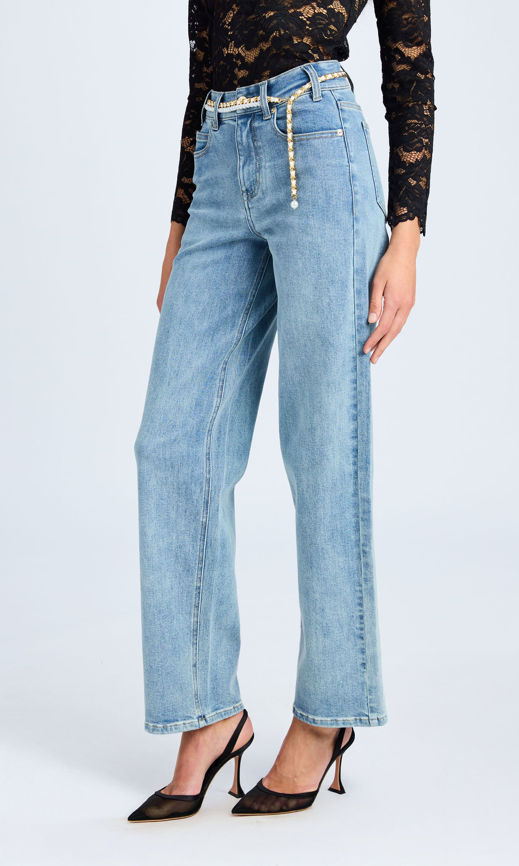 A woman wearing bahama blue jeans with a pearl belt, posed sideways, emphasizing her chic style