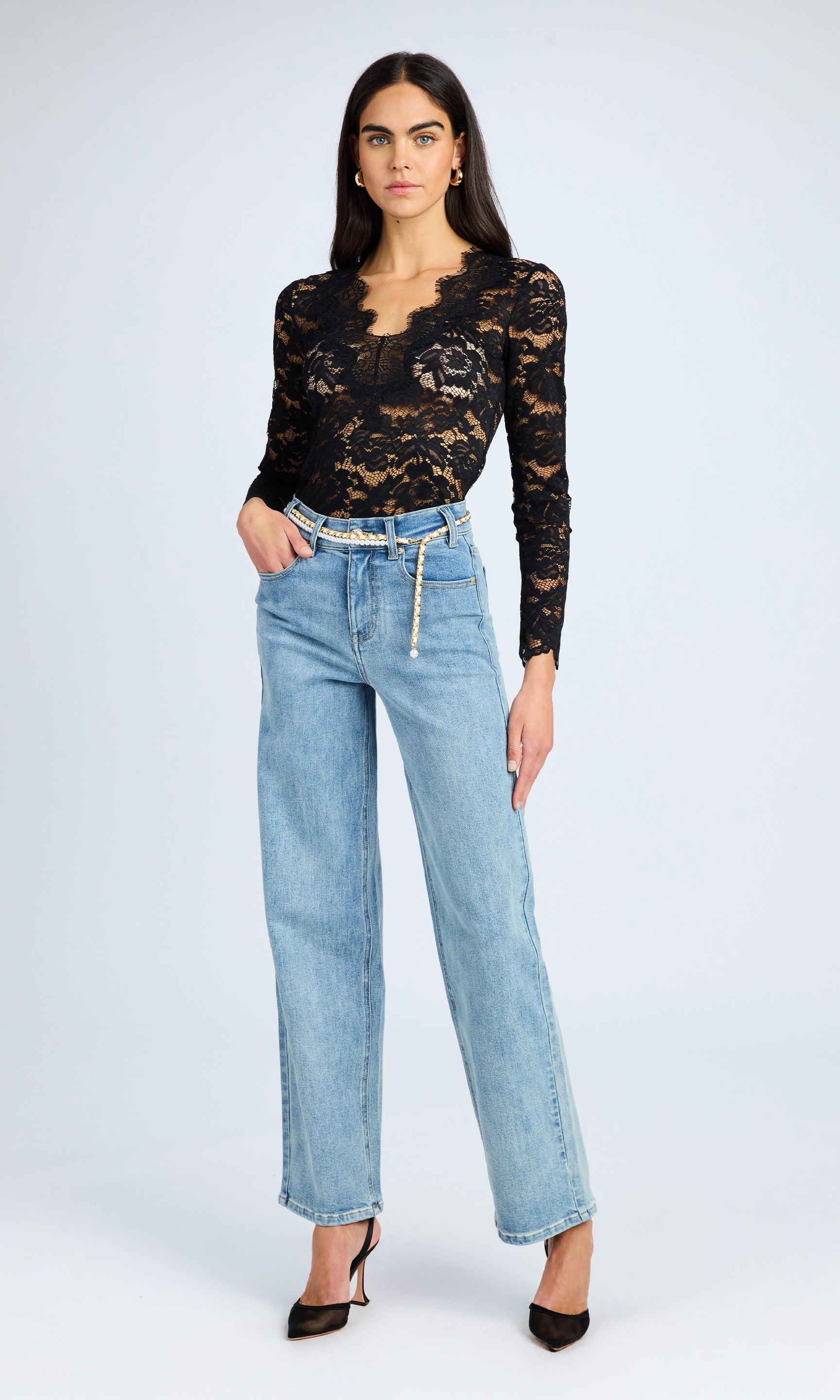 Model stands confidently in a navy sweater and bahama blue jeans, showcasing a pearl belt that adds elegance to the casual look.