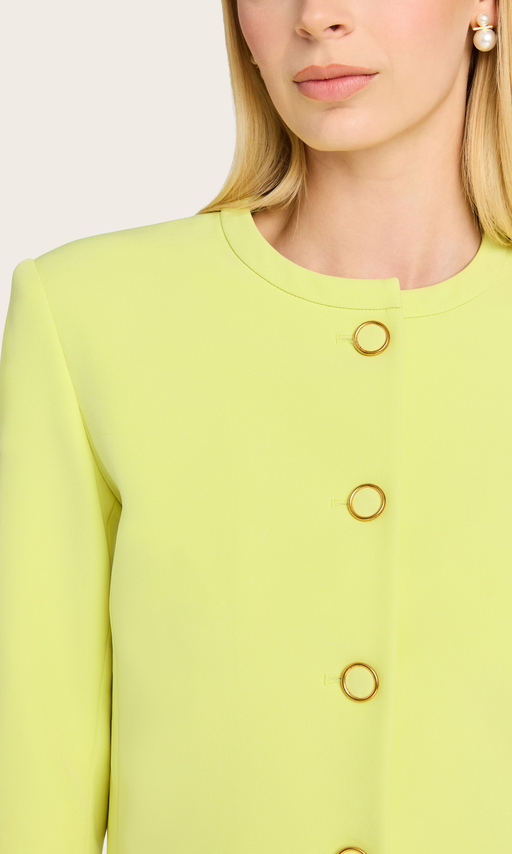 The model wears the Monte Crepe Jacket in a close-up image, showcasing its bright hue, gold-tone buttons, and crisp collarless neckline for a polished summer feel.
